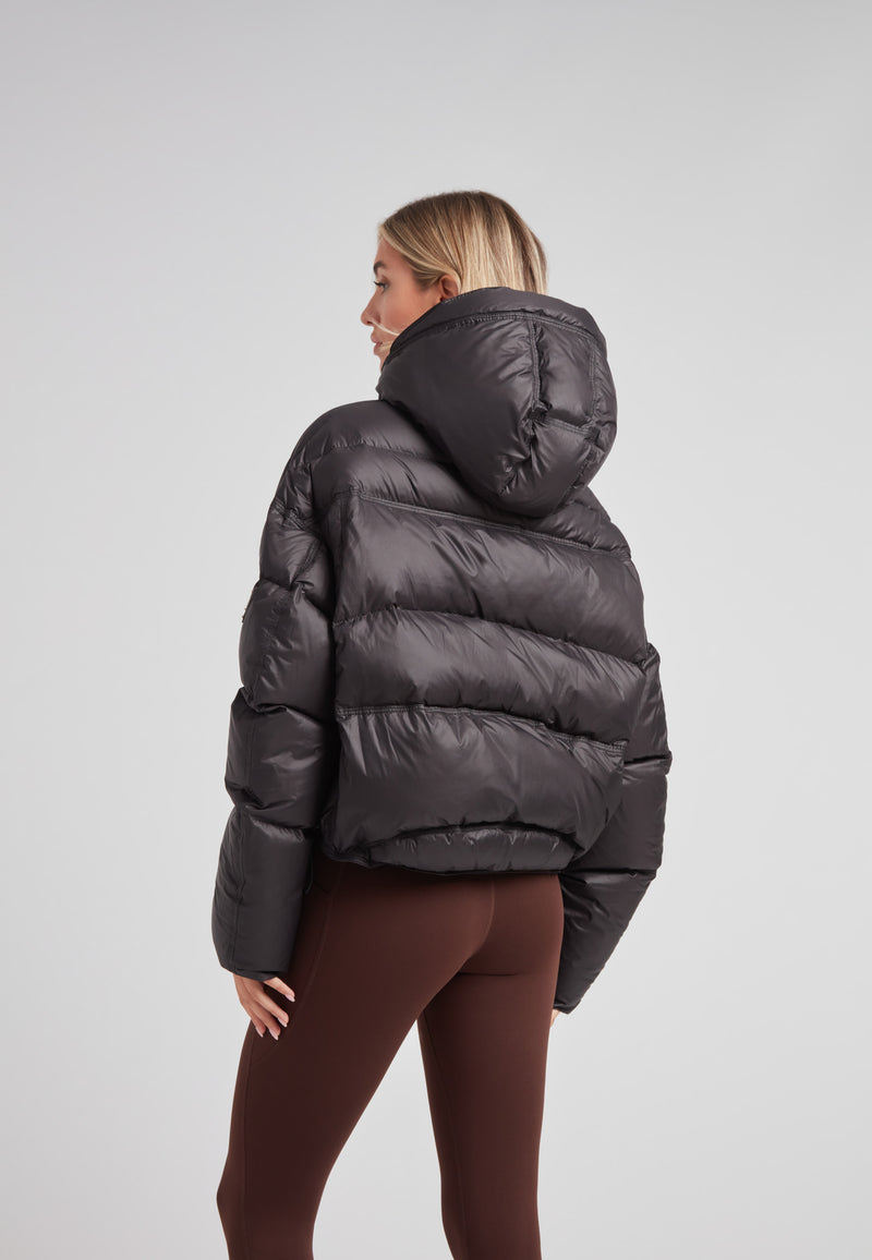 Model wearing a cropped puffer in black with adjustable coverage, showcasing the back view and removable hood.