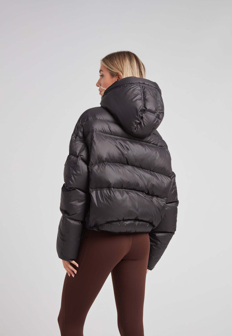 Model wearing a cropped puffer in black with adjustable coverage, showcasing the back view and removable hood.