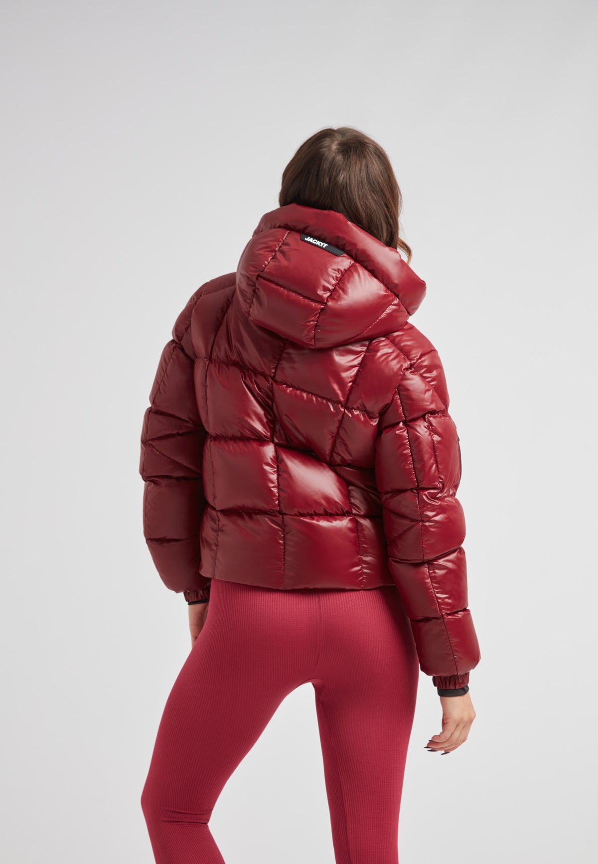 Back view of a woman wearing the EZ Boxed Crop Down Puffer Jacket Lux Cranberry with matching leggings.