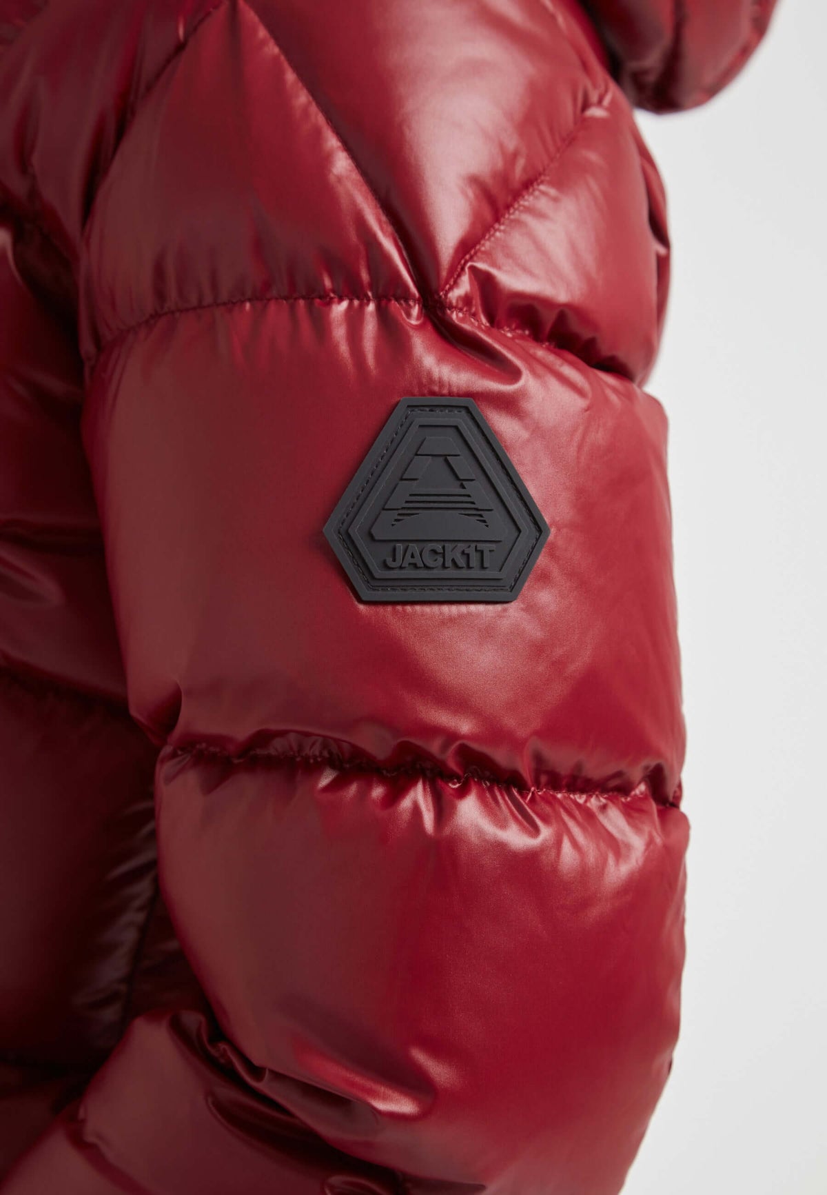 Close-up of the sleeve of a short down puffer jacket women in Lux Cranberry, featuring a logo patch.