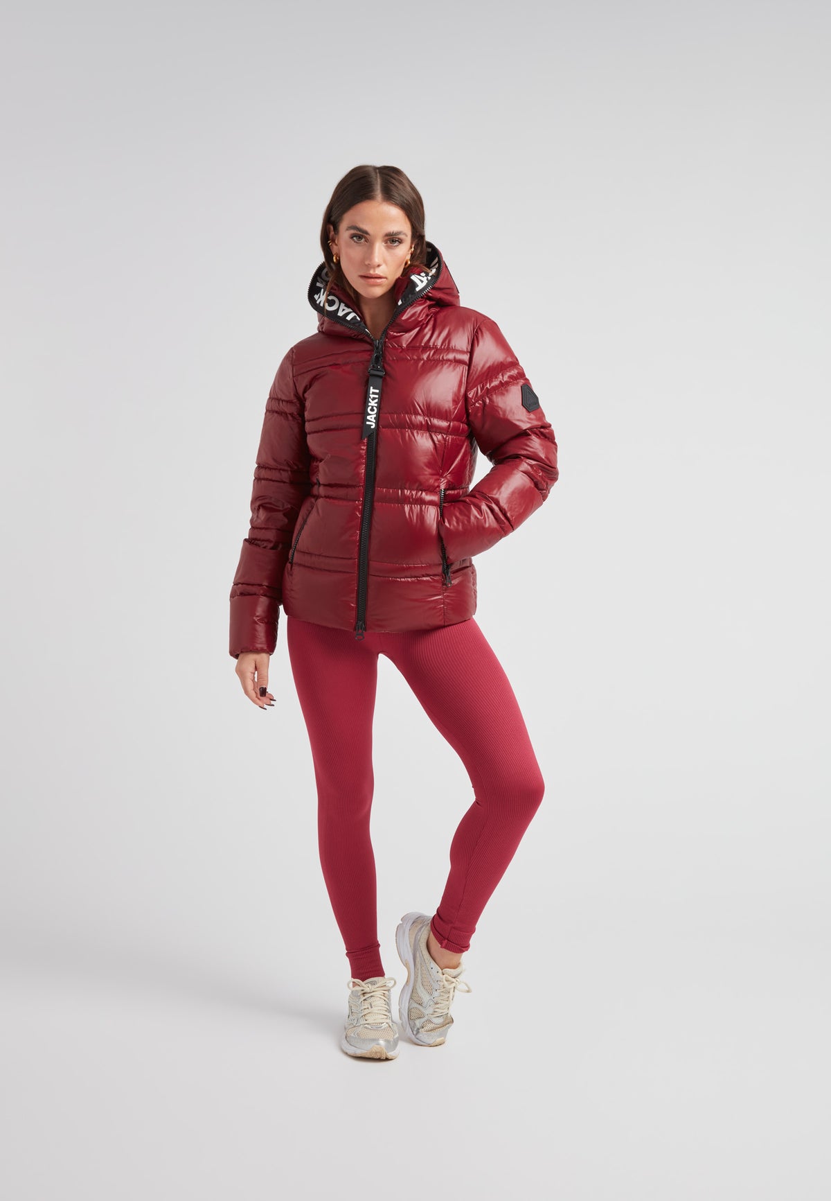 Model wearing R4D Tramline Puffer Racer Jacket Lux Cranberry over red leggings, showcasing stylish warmth and comfort.