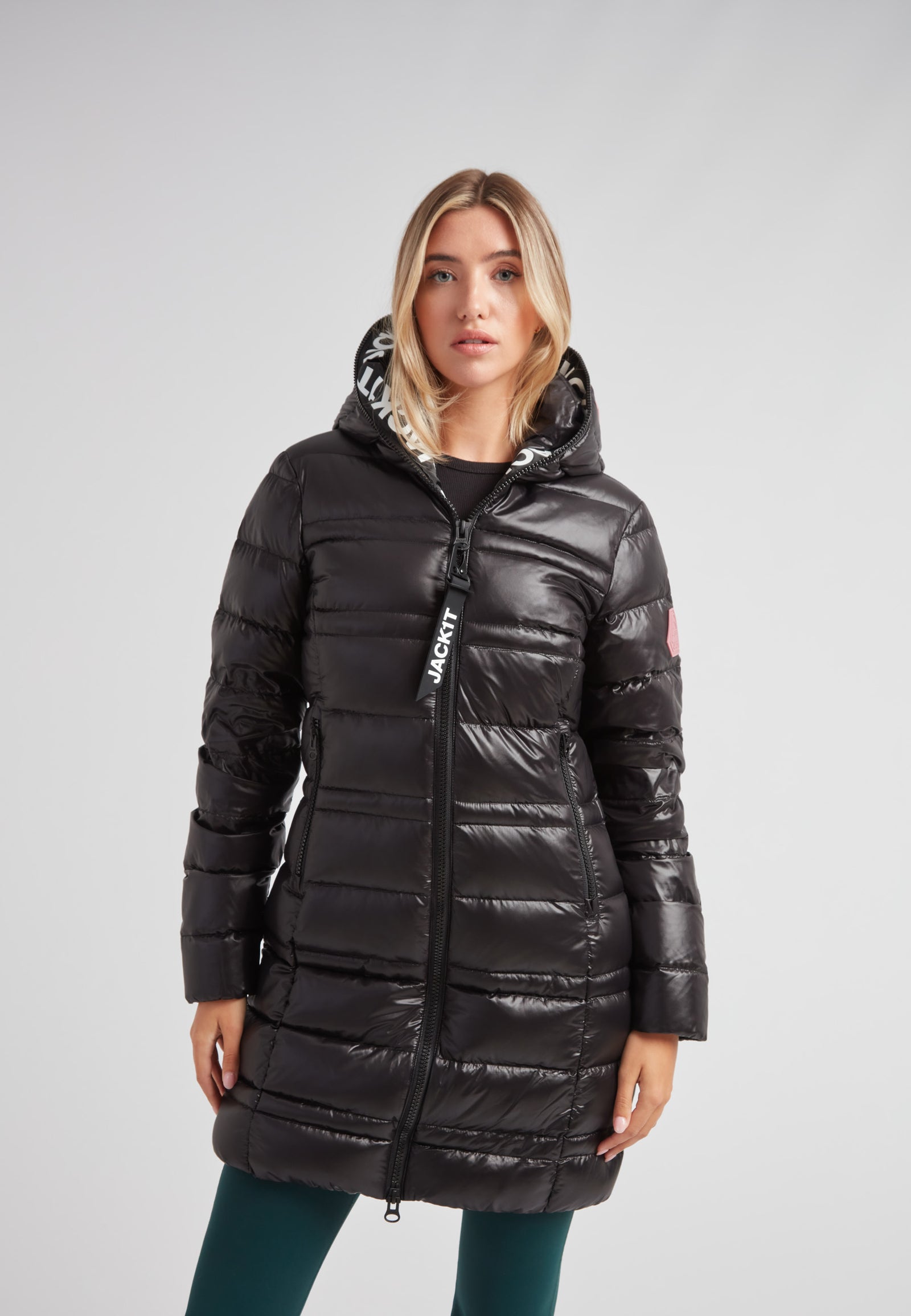 Woman wearing the R4D Tramline Down Coat Lux Black with hood, showcasing its sleek design and style.