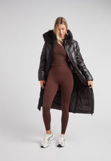 Model wearing Diamond Belted Extra Long Down Coat Lux Black with faux fur hood and activewear underneath.