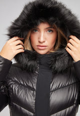 Model wearing the Diamond Belted Extra Long Down Coat Lux Black with faux fur hood.