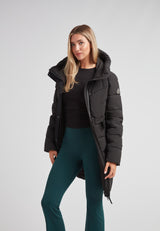 Woman wearing Diamond Belted Down Coat Matt Black with a hood, styled with green pants, showcasing winter fashion.