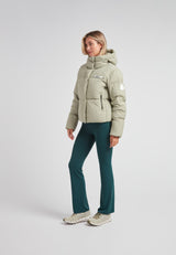 Woman wearing the Star Shower Down Puffer Jacket Sage, paired with green pants and stylish sneakers.