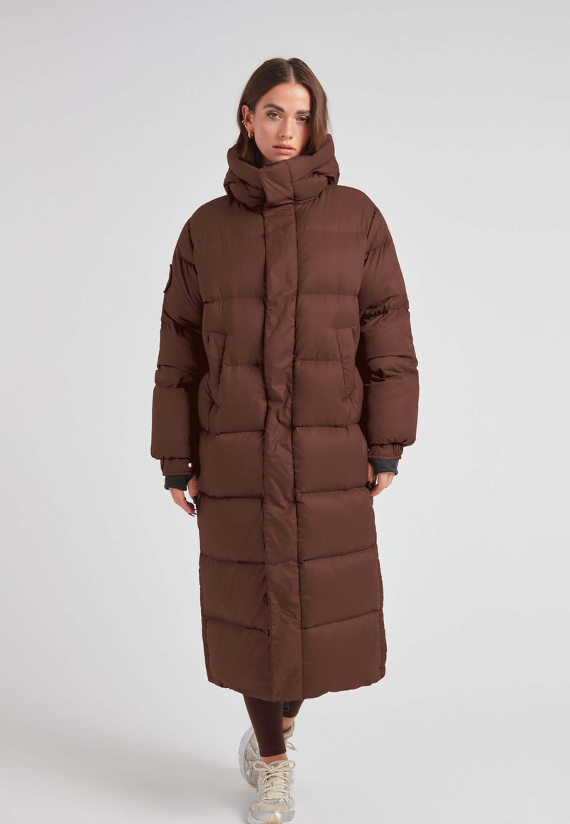 Cocoon Ultra Long Down Coat Mid Brown displayed on a model, featuring an oversized silhouette and a cozy hood.