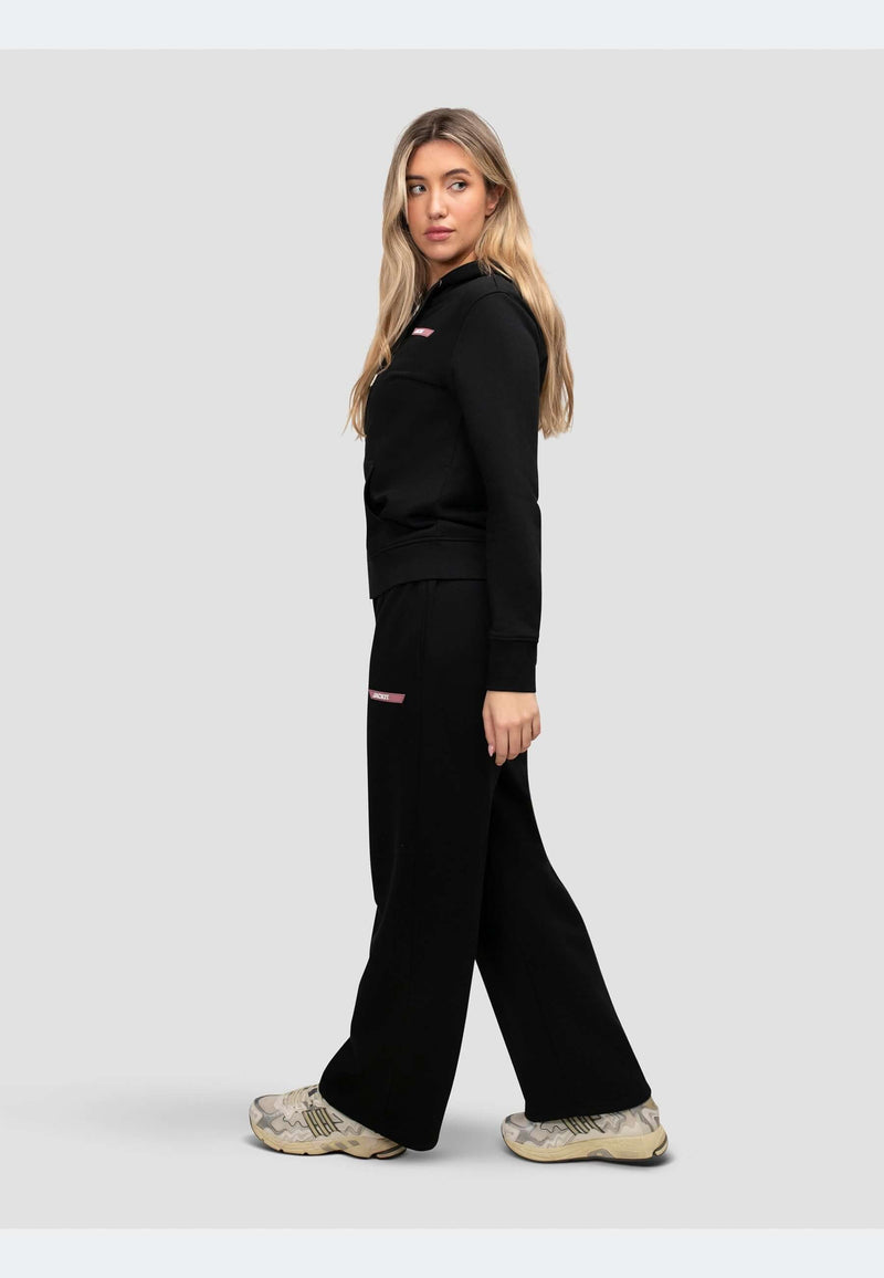 Model wearing a zip through black hoodie with relaxed fit and matching pants, showcasing a sporty look.
