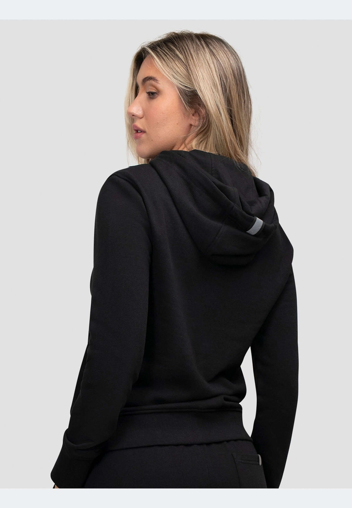 Woman wearing a zip through black hoodie from the back, showcasing its relaxed fit and premium fabric.