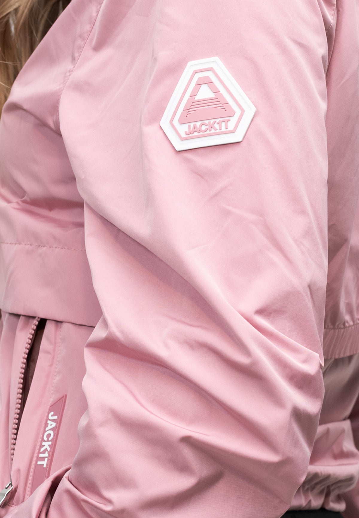 Close-up of a women's pink windbreaker featuring a logo on the sleeve and a lightweight fabric for spring weather.