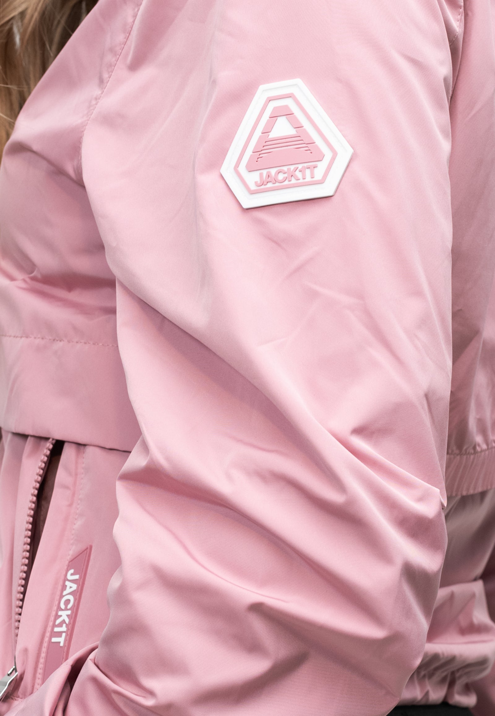 Close-up of a women's pink windbreaker featuring a logo on the sleeve and a lightweight fabric for spring weather.