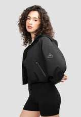Ladies Cropped Black Jacket displayed on a model with curly hair, featuring an adjustable hood and zip pockets.
