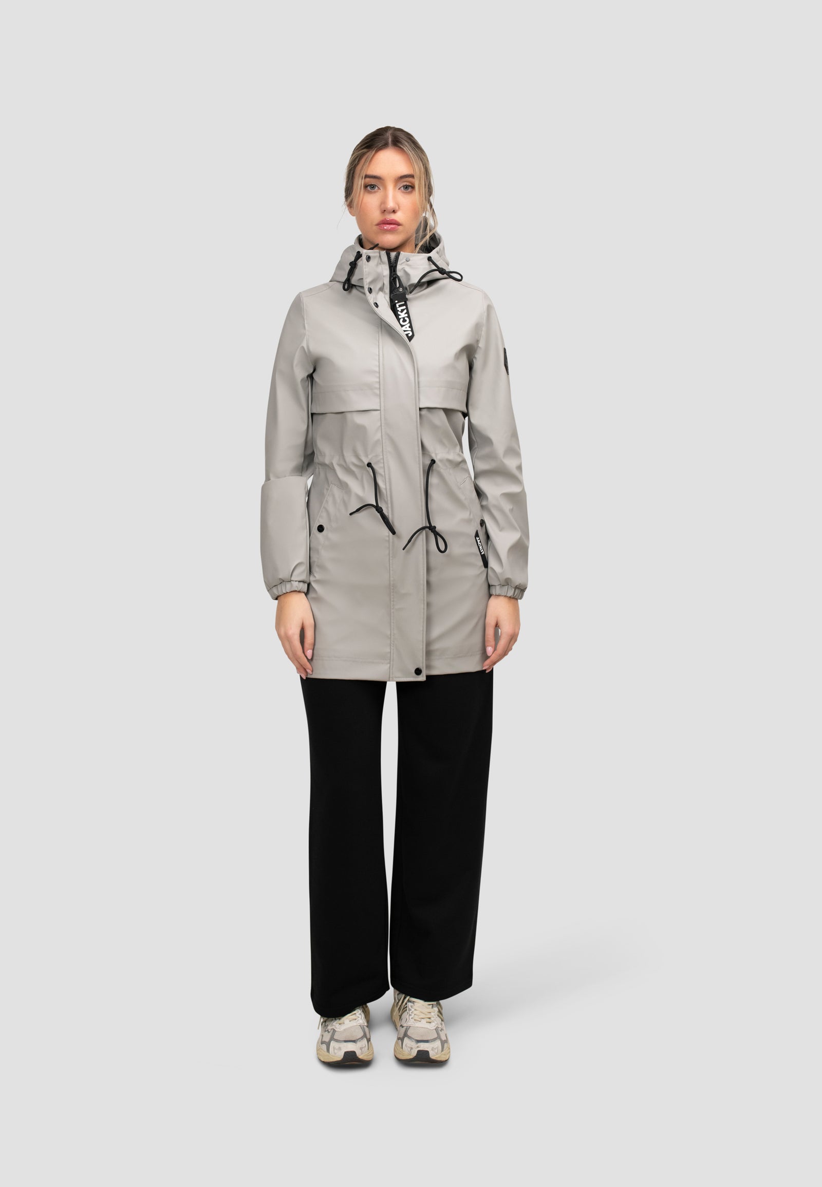 Model wearing a women's grey raincoat with cape in dusty light grey, featuring a sculptural silhouette and drawstring details.