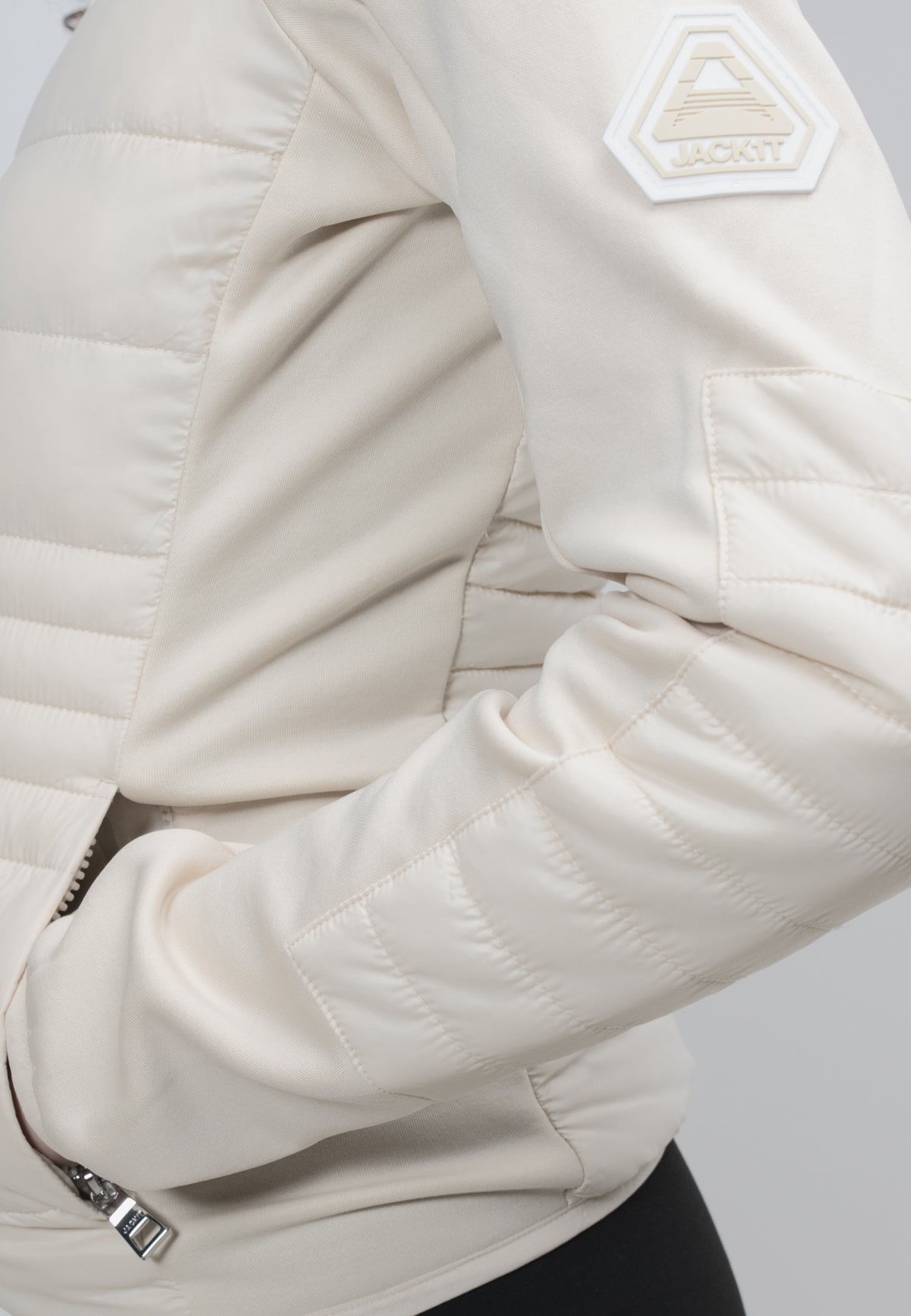 Close-up of a women's cream hooded jacket showcasing the quilted texture and logo detail.