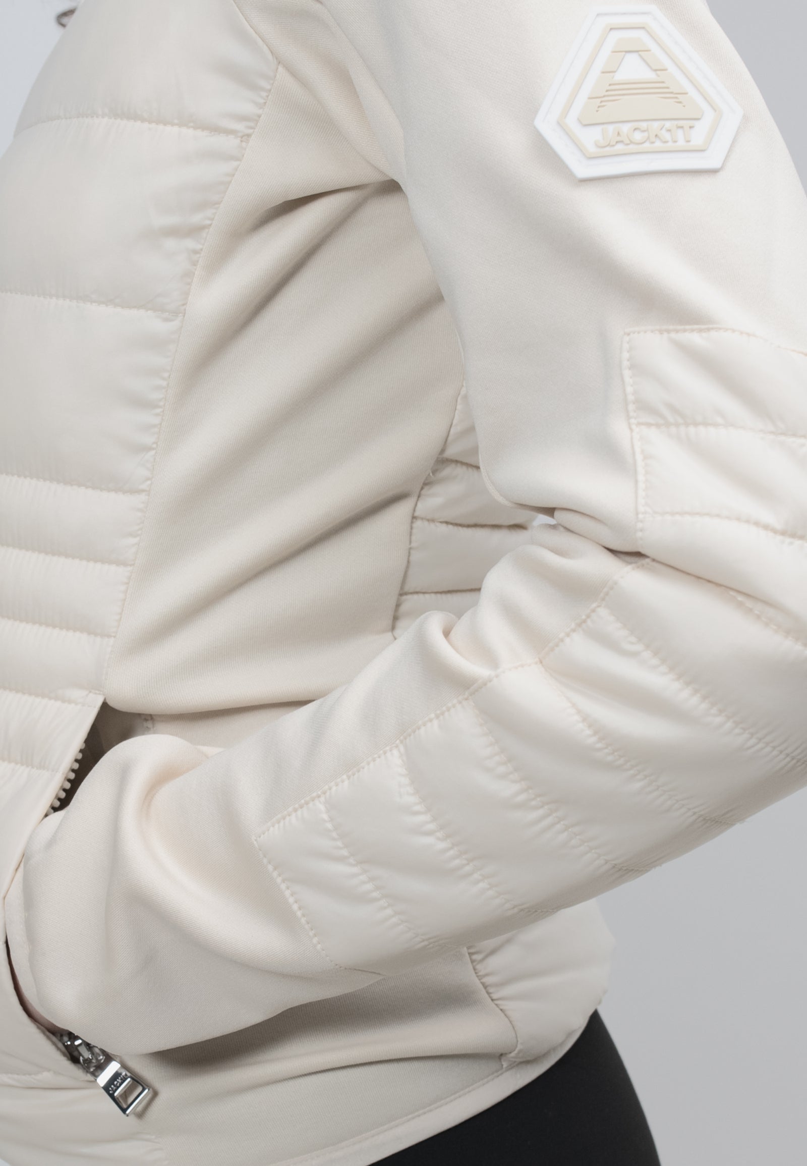 Close-up of a women's cream hooded jacket showcasing the quilted texture and logo detail.