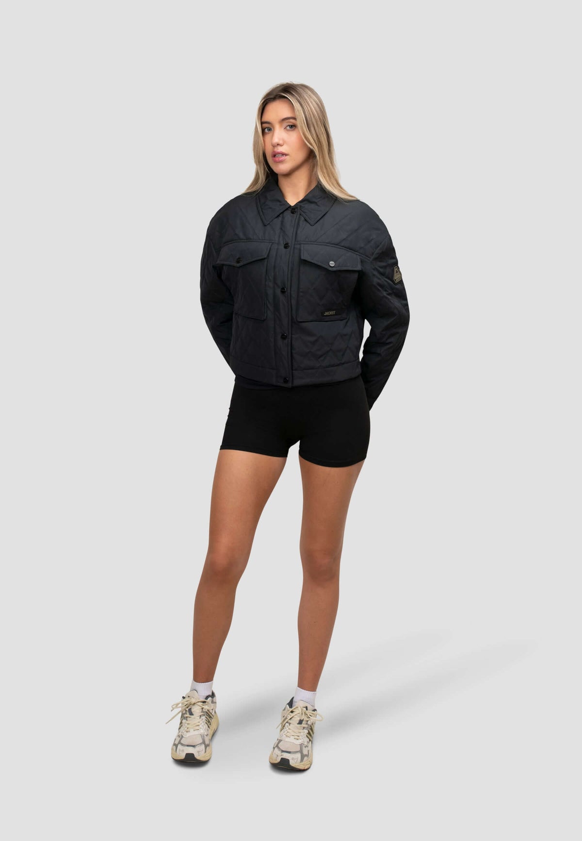 Model wearing women's black quilted shirt jacket in a relaxed fit, styled with shorts and sneakers.