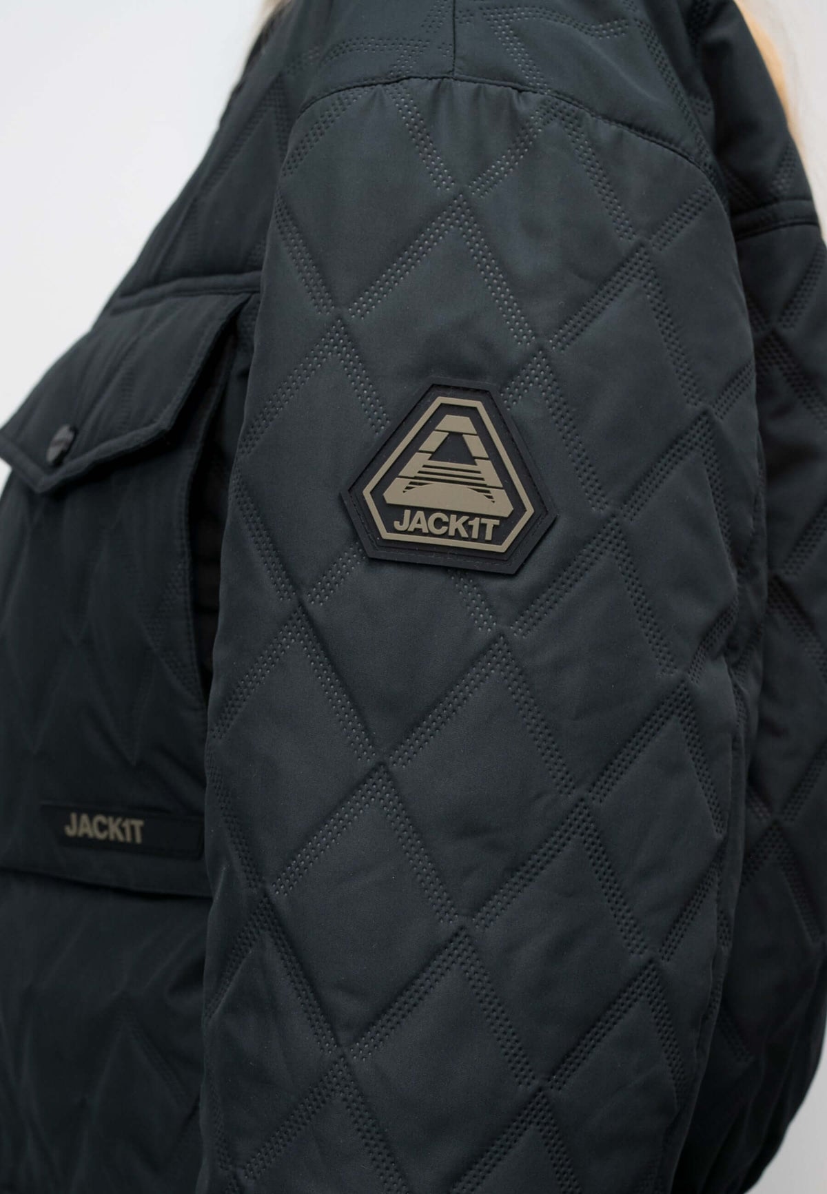 Close-up of the women's black quilted shirt jacket showing the diamond pattern and logo detail.