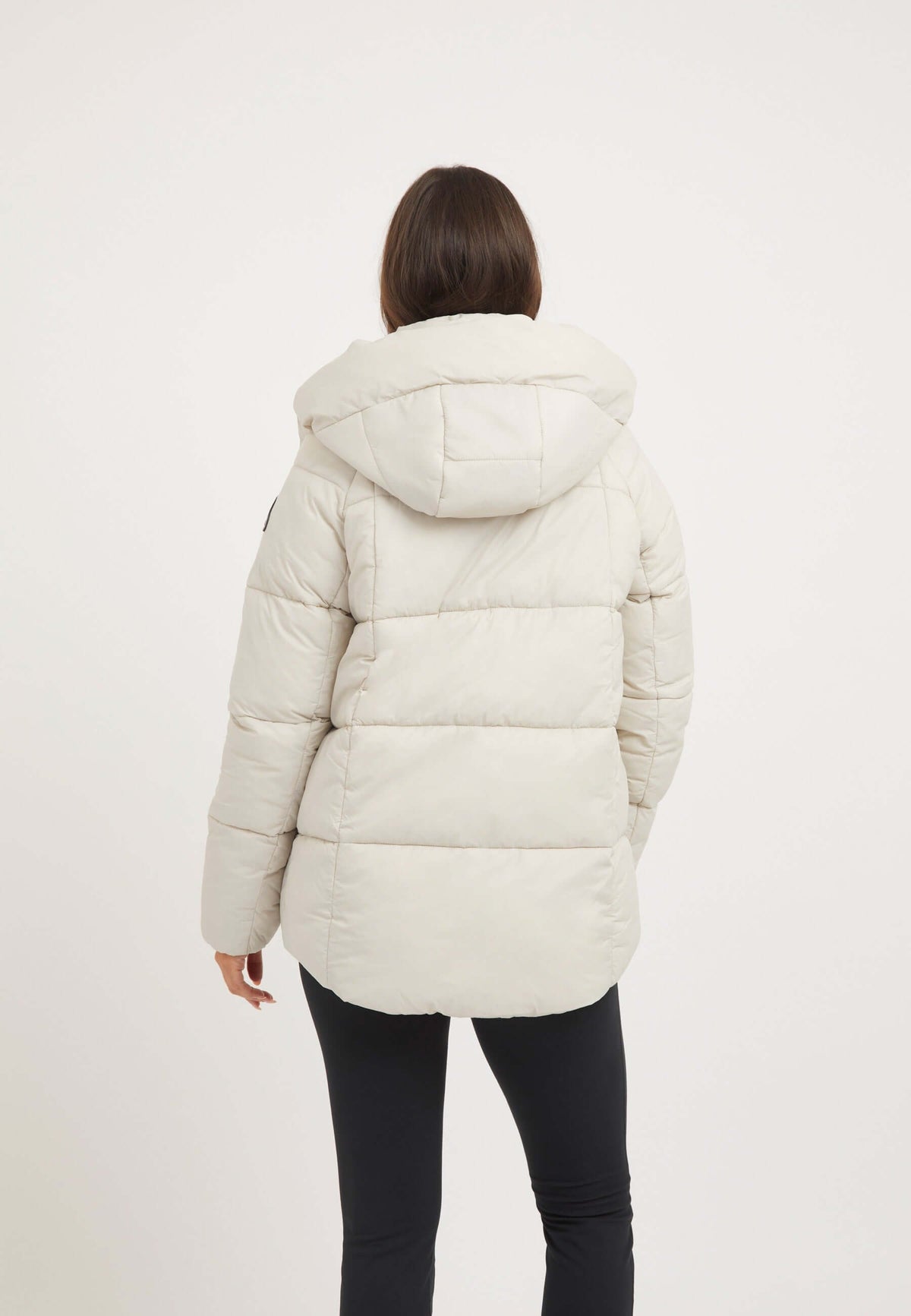 Back view of a woman wearing a lightweight puffer jacket stone with an adjustable hood.