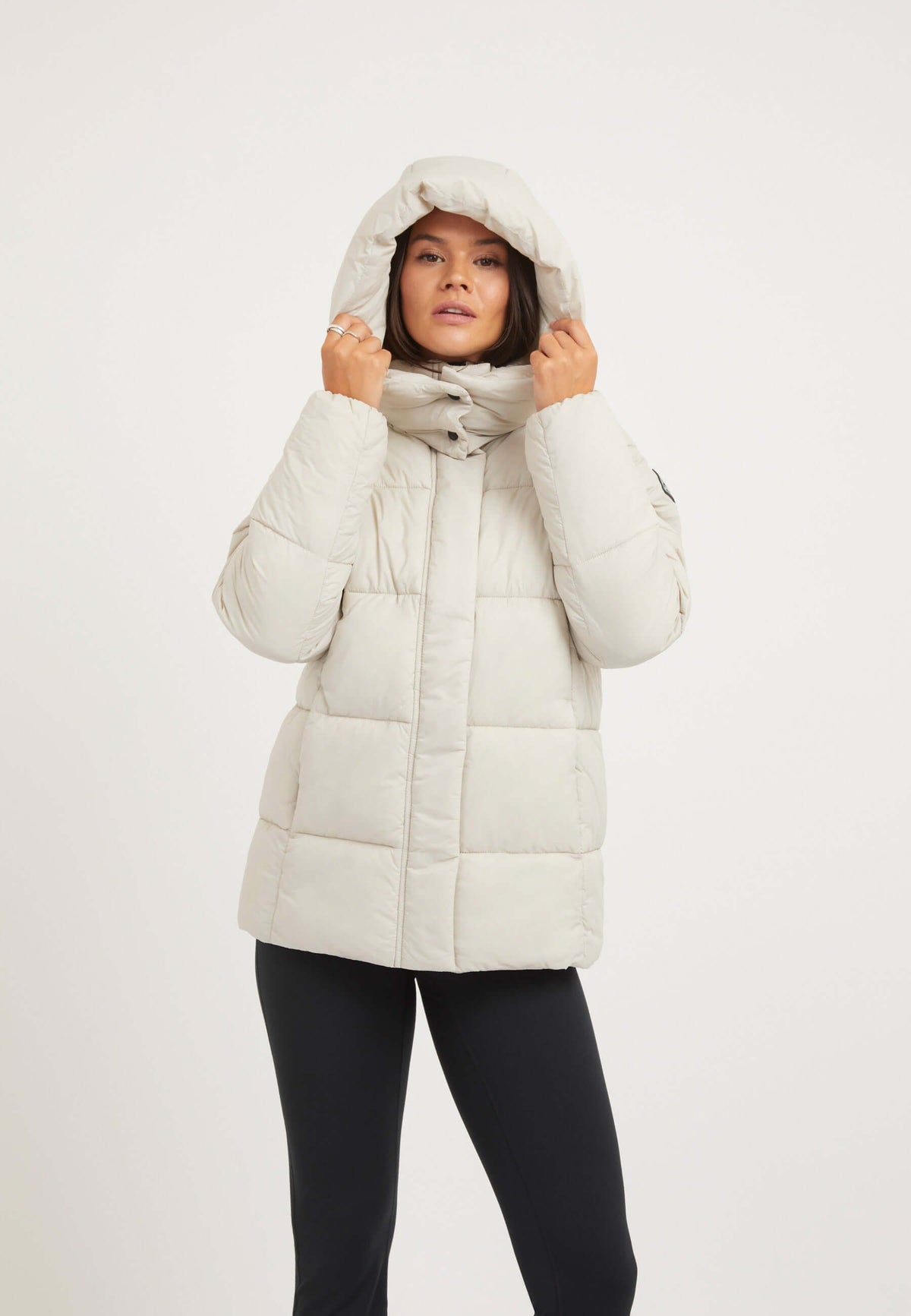 Woman wearing the Cloud Prime Jacket Stone, a tapered puffer jacket stone with an adjustable hood and premium synthetic insulation.