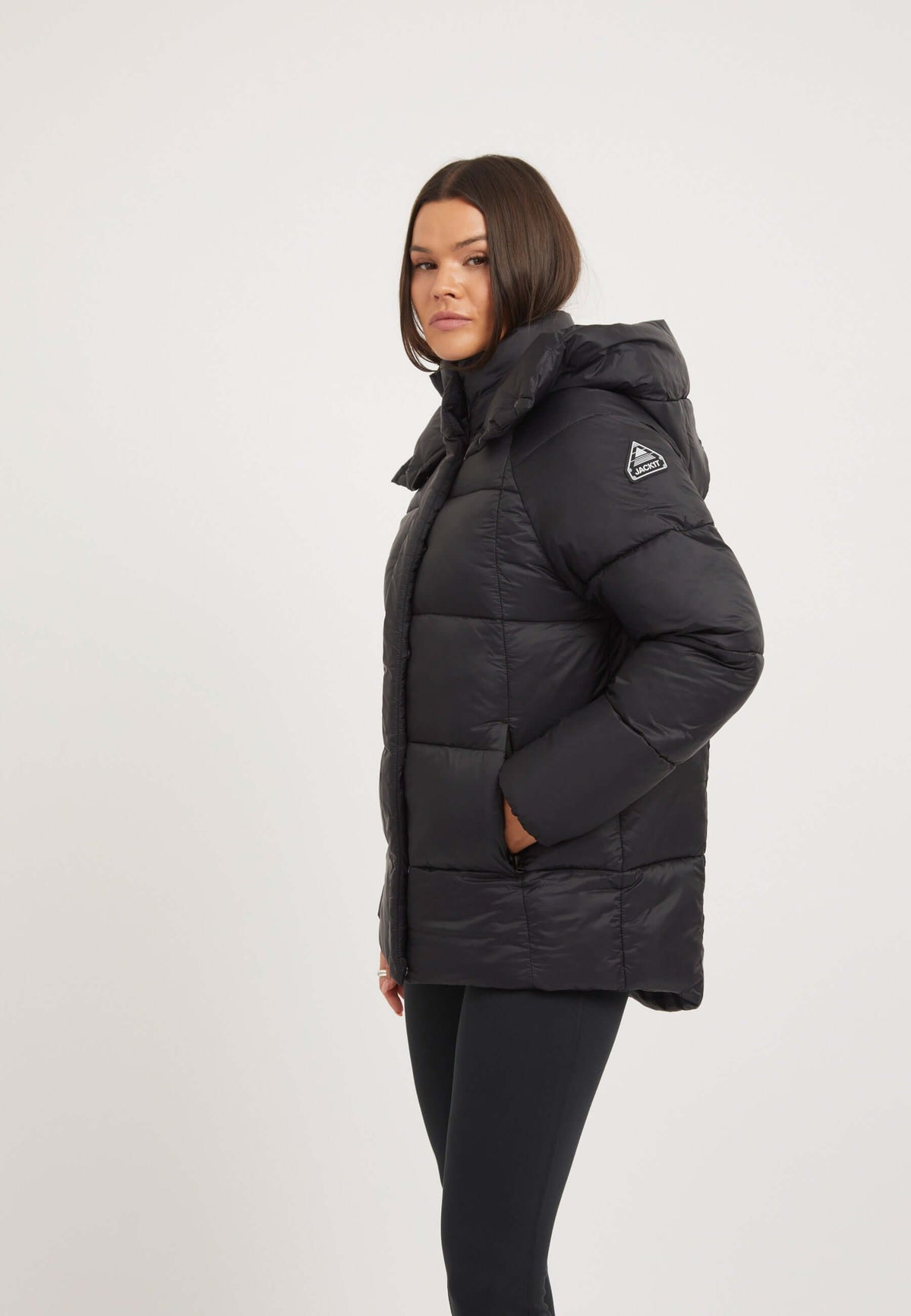 Womens black puffer jacket displayed on model with adjustable hood and reflective badge.