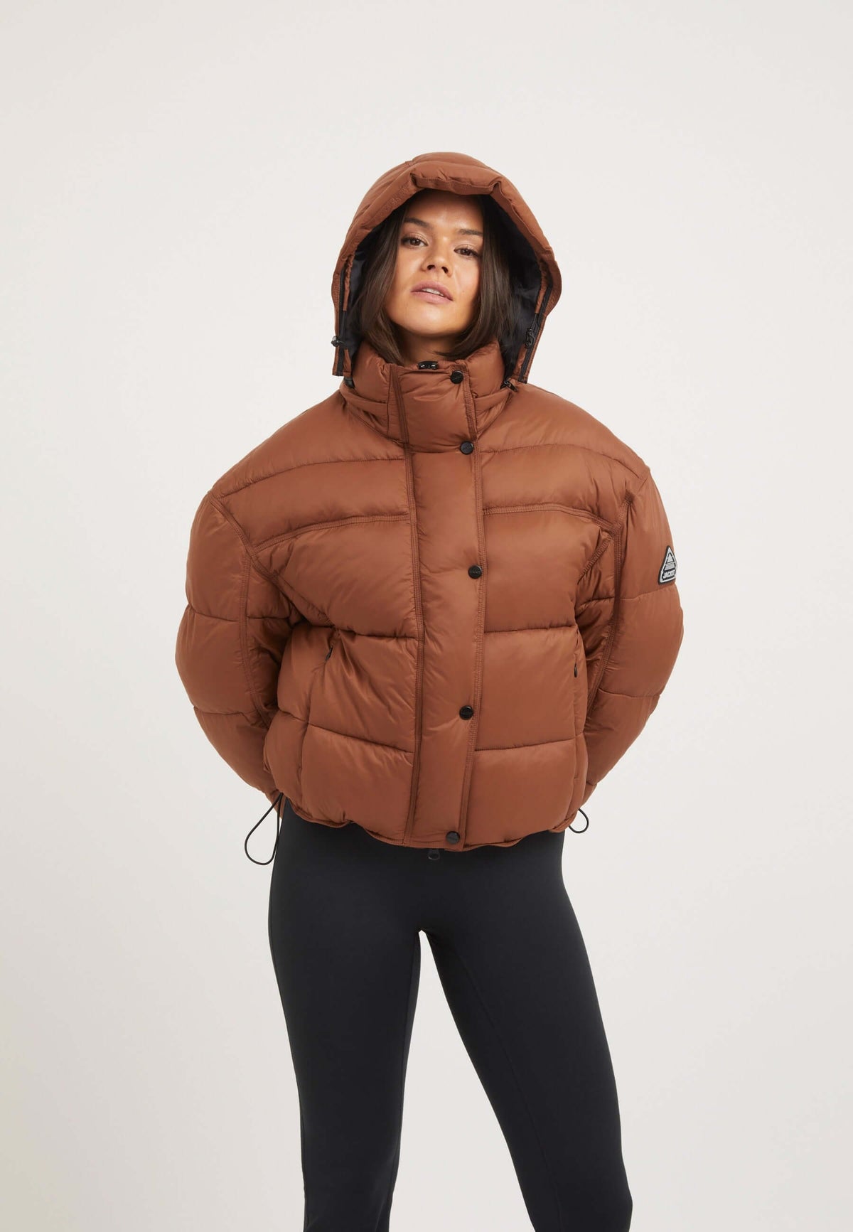 Model wearing a Cloud Boss Womens Puffer Jacket Brown in mocha brown color with removable hood and oversized silhouette.