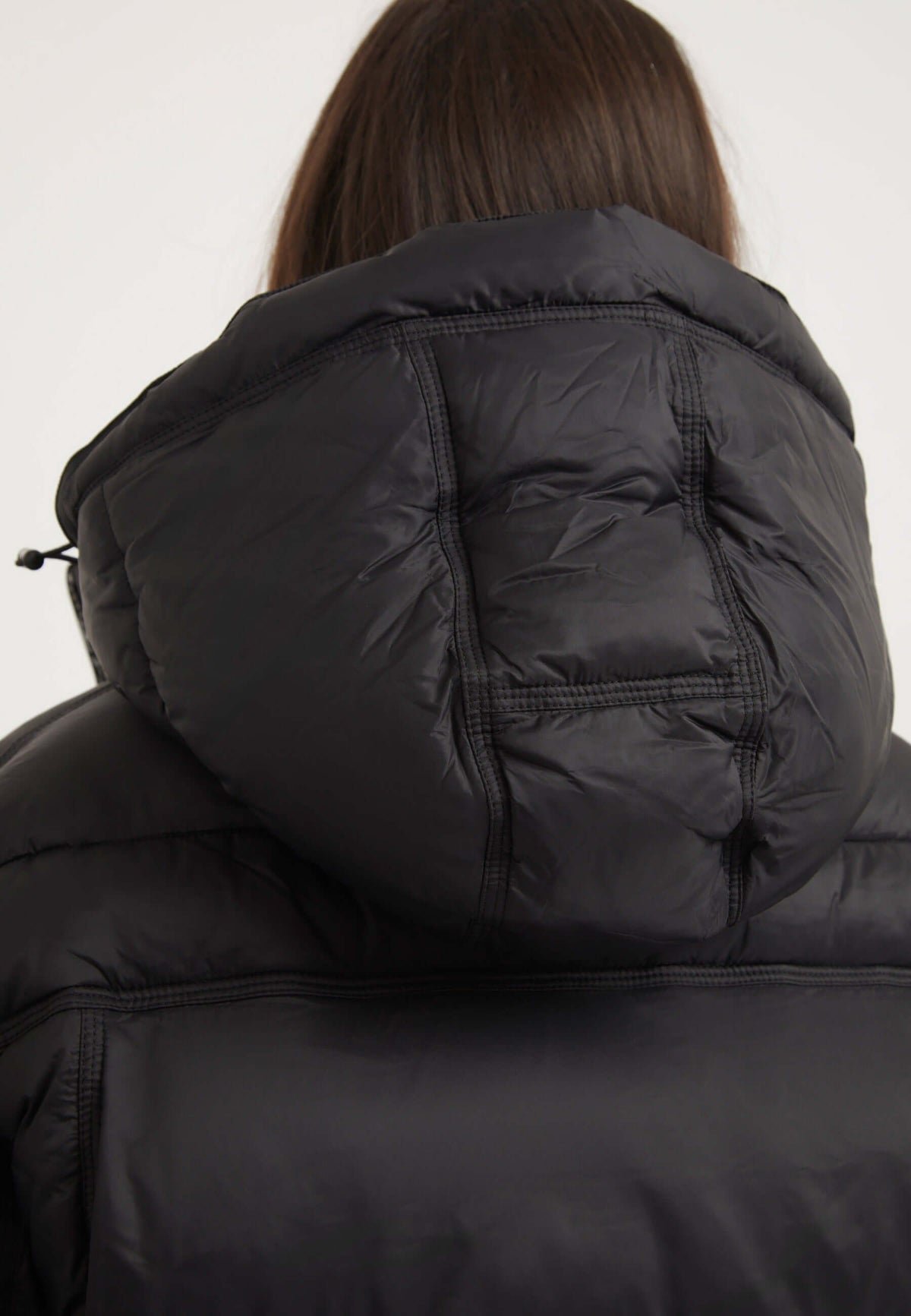 Back view of a woman wearing a Cloud Boss Jacket Black, featuring a removable hood and puffer design. womens black puffer jacket.