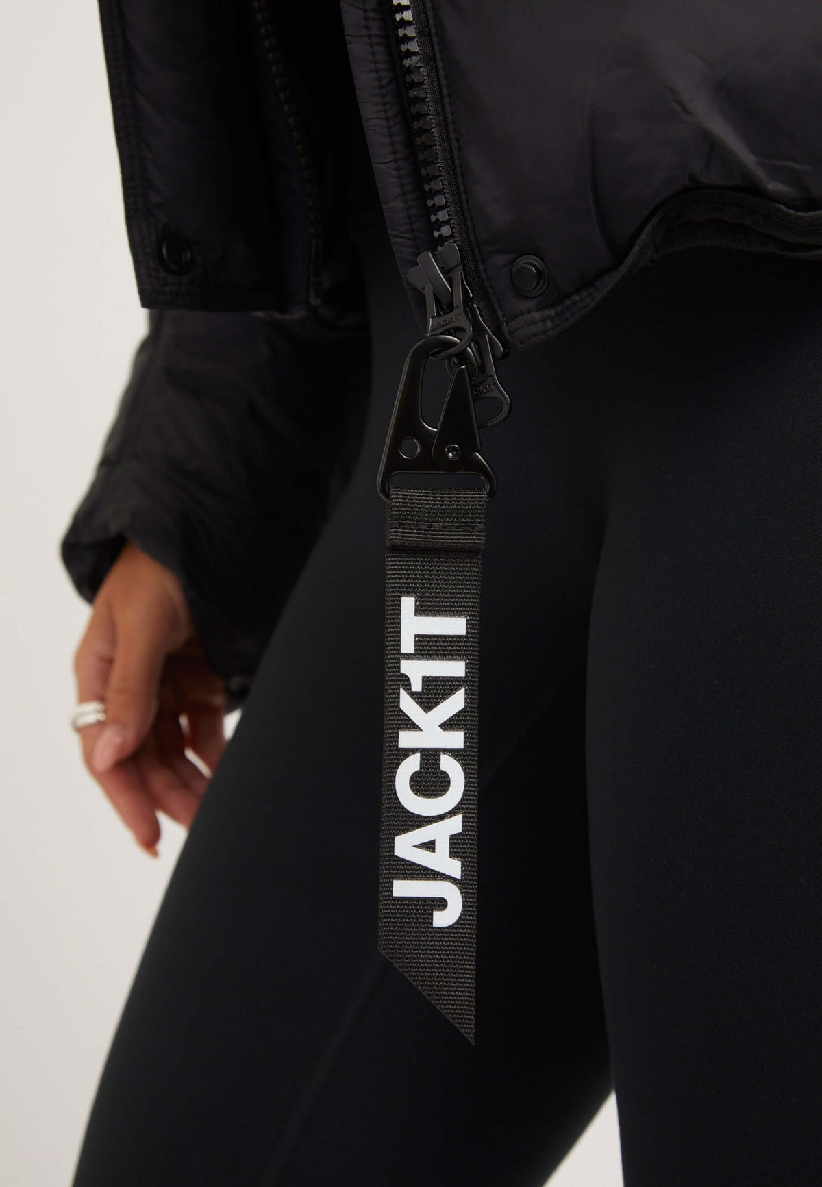 Close-up of a model wearing a womens black puffer jacket with a JACKIT tag on the zipper.