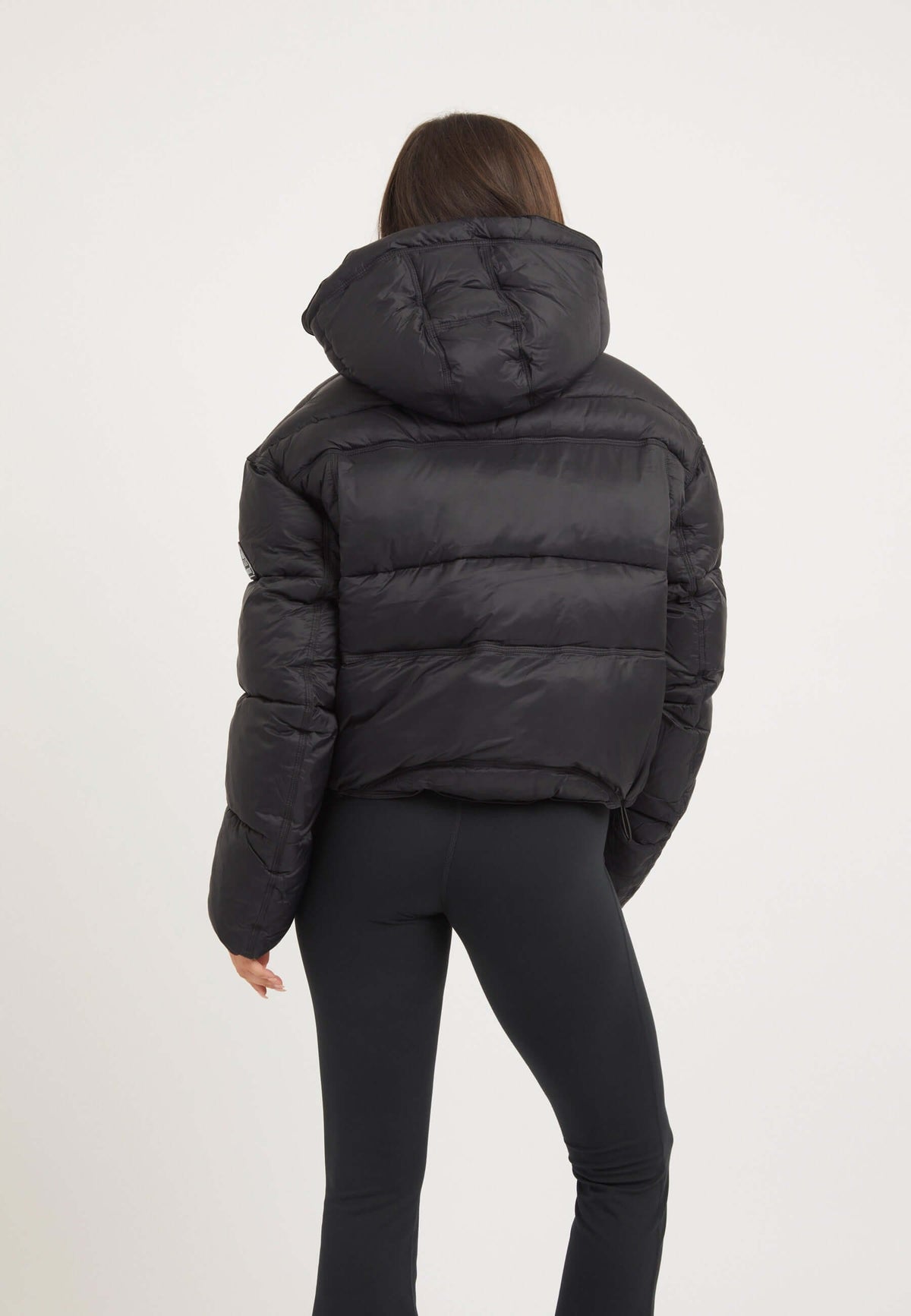 Woman wearing a womens black puffer jacket from the back, showcasing its oversized silhouette and removable hood.