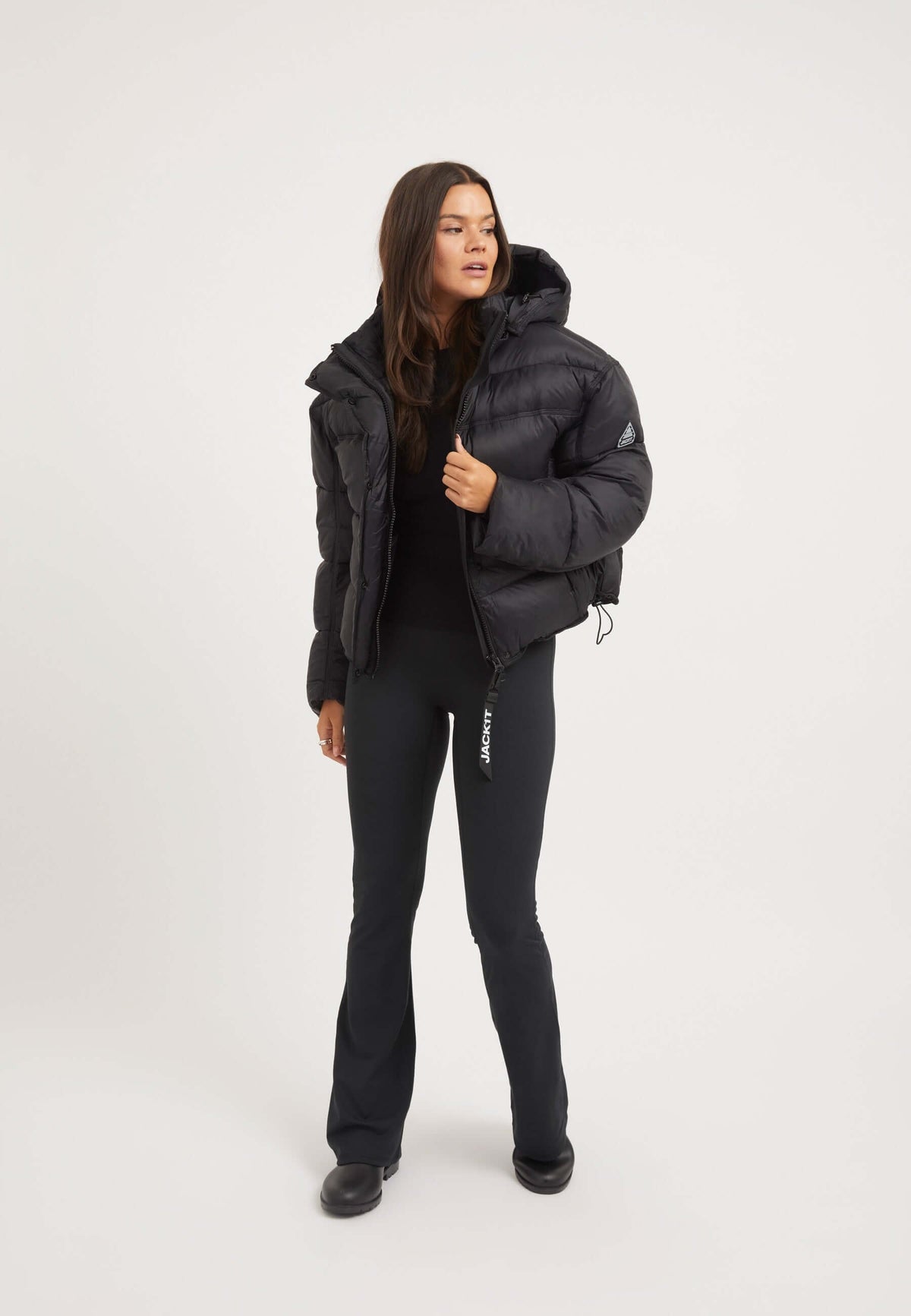 Model wearing a womens black puffer jacket with oversized silhouette and removable hood.
