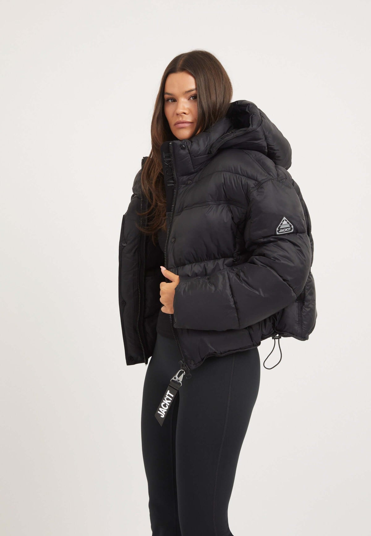 Woman wearing Cloud Boss Jacket Black, an oversized womens black puffer jacket with removable hood and reflective badge.