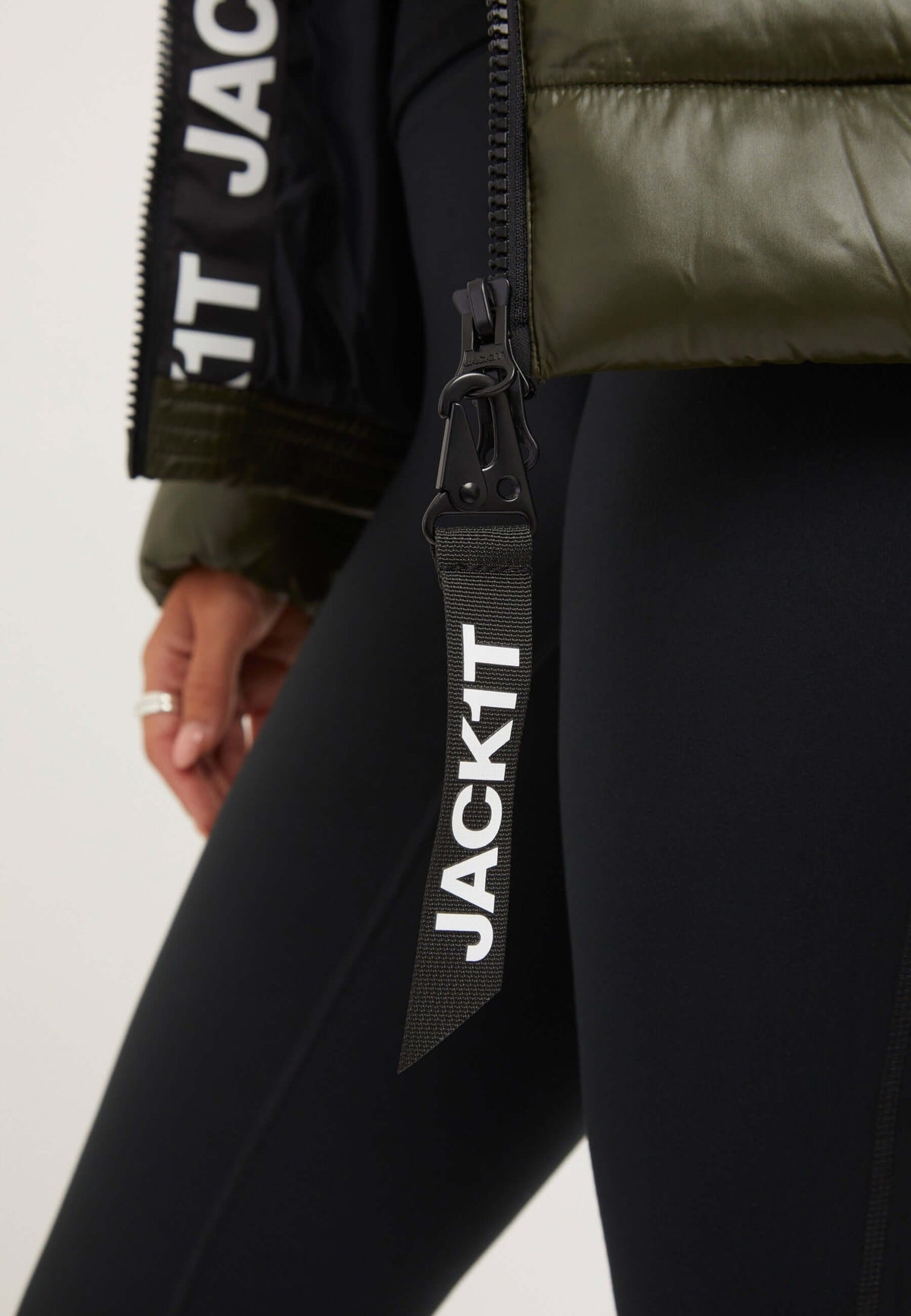 Close-up of R3D Slick Racer Jacket Olive showing zipper detail and JACK1T tag; a fitted puffer jacket with sleek design.