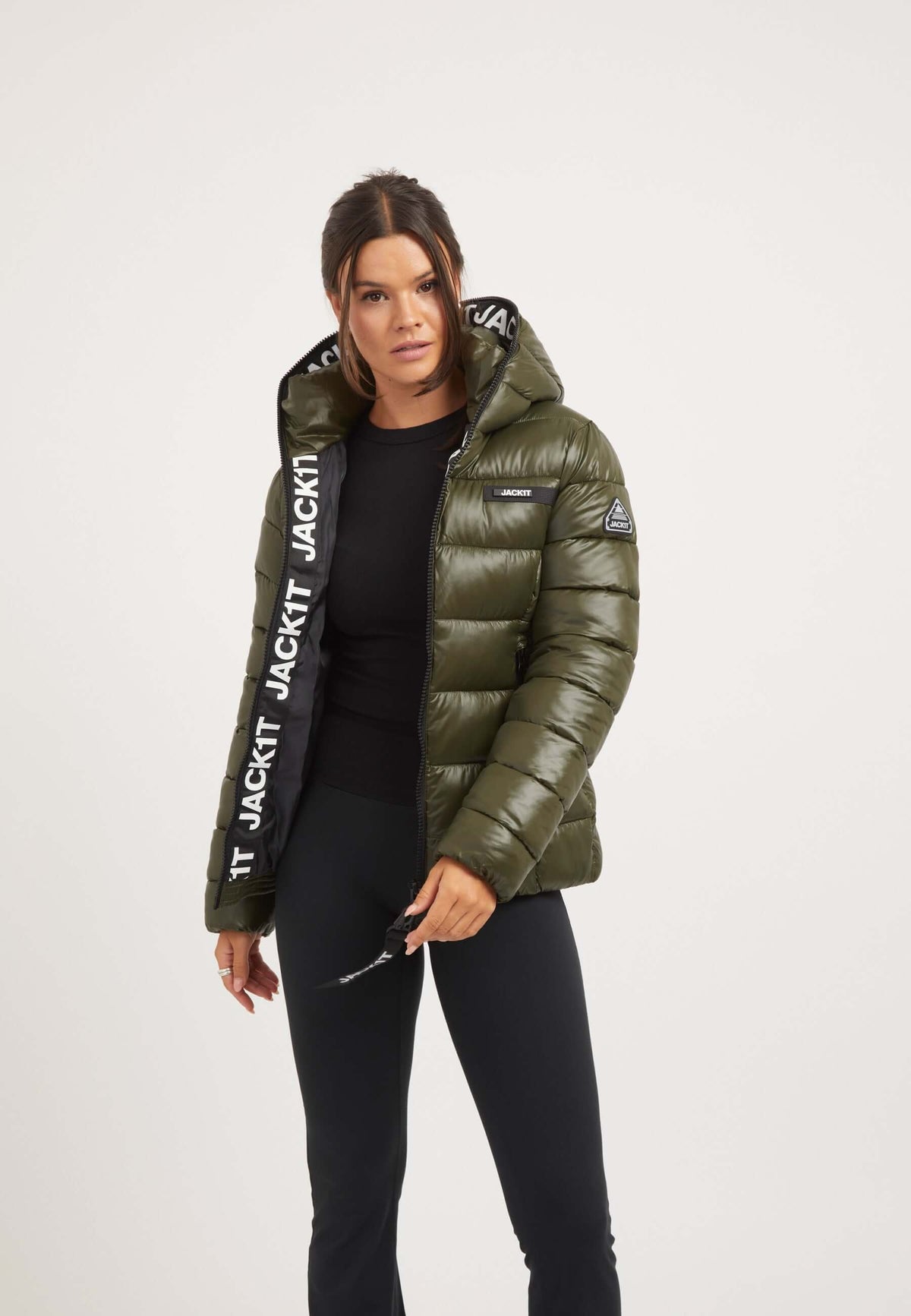 Woman wearing R3D Slick Racer Jacket Olive, a fitted puffer jacket with a hood and stylish reflective details.