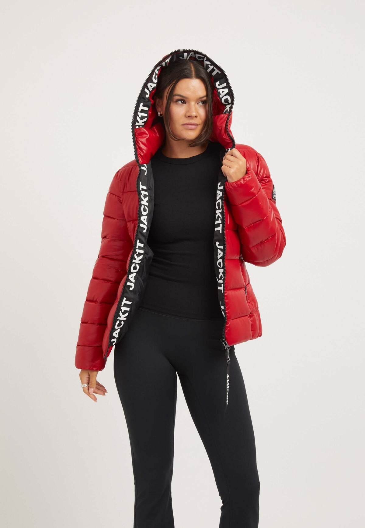 Short red jacket with a hood, featuring a puffer design and stylish branding, worn by a model in a casual outfit.