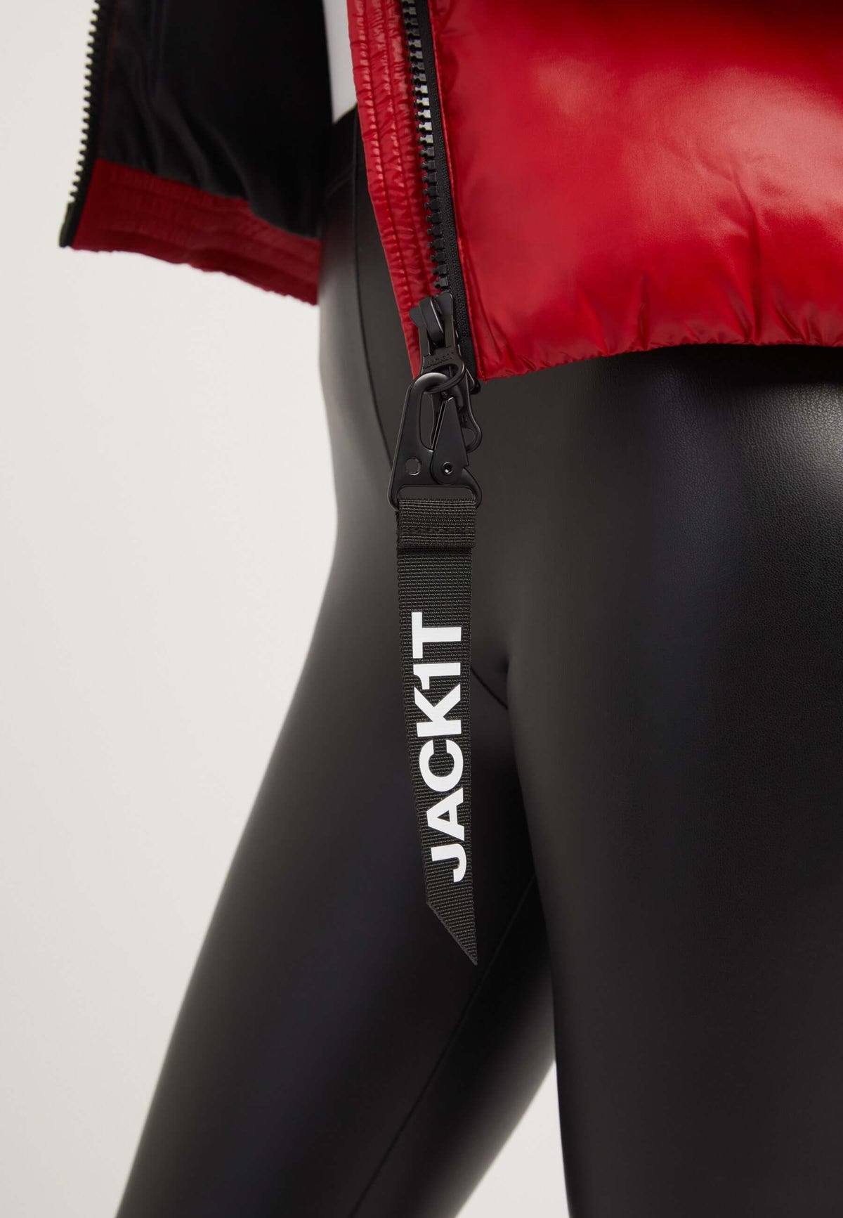 Close-up of red puffer jacket and black leggings, showcasing zipper tag labeled JACKIT.