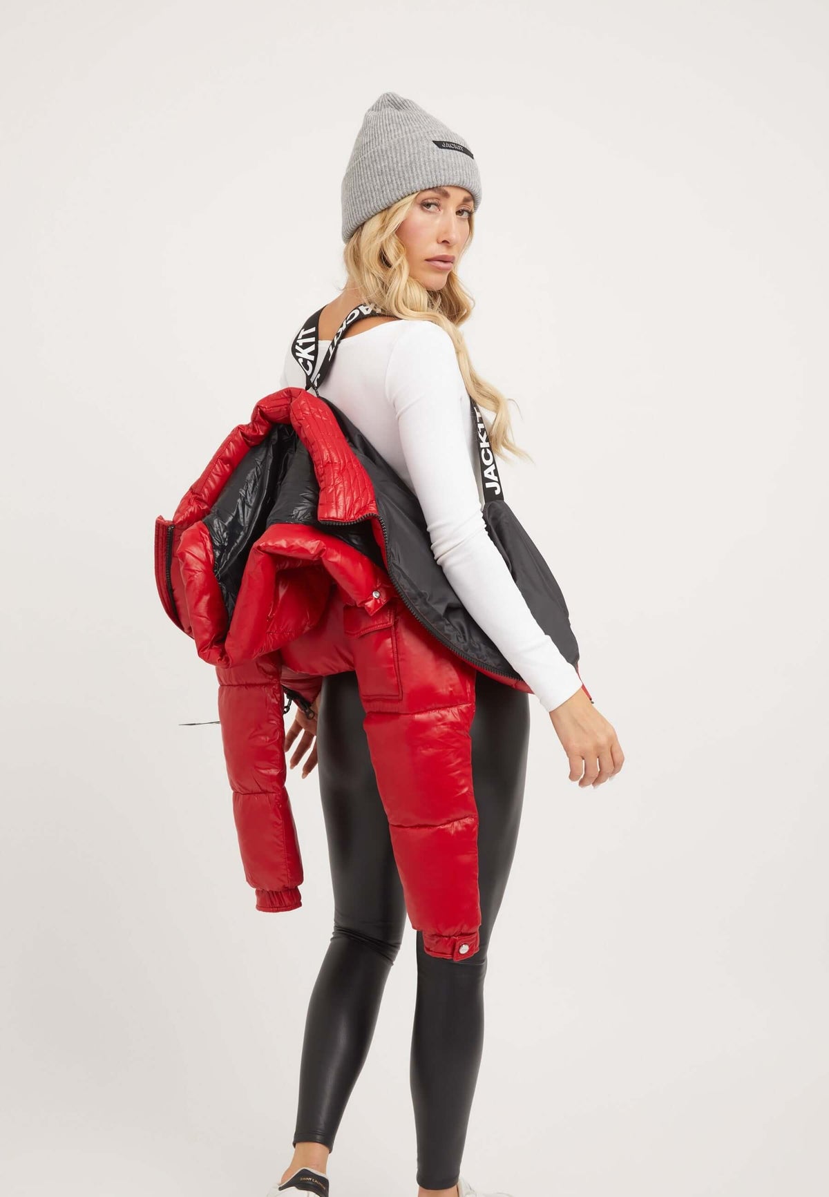 Model wearing a red puffer jacket with removable hood, paired with leggings and a stylish beanie.