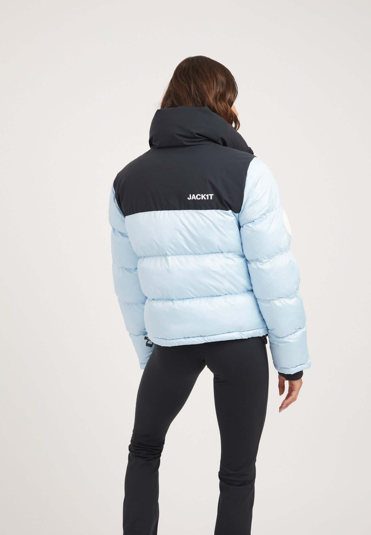 Back view of a woman wearing a Powder Blue and Black Funnel neck jacket with premium insulation and logo.