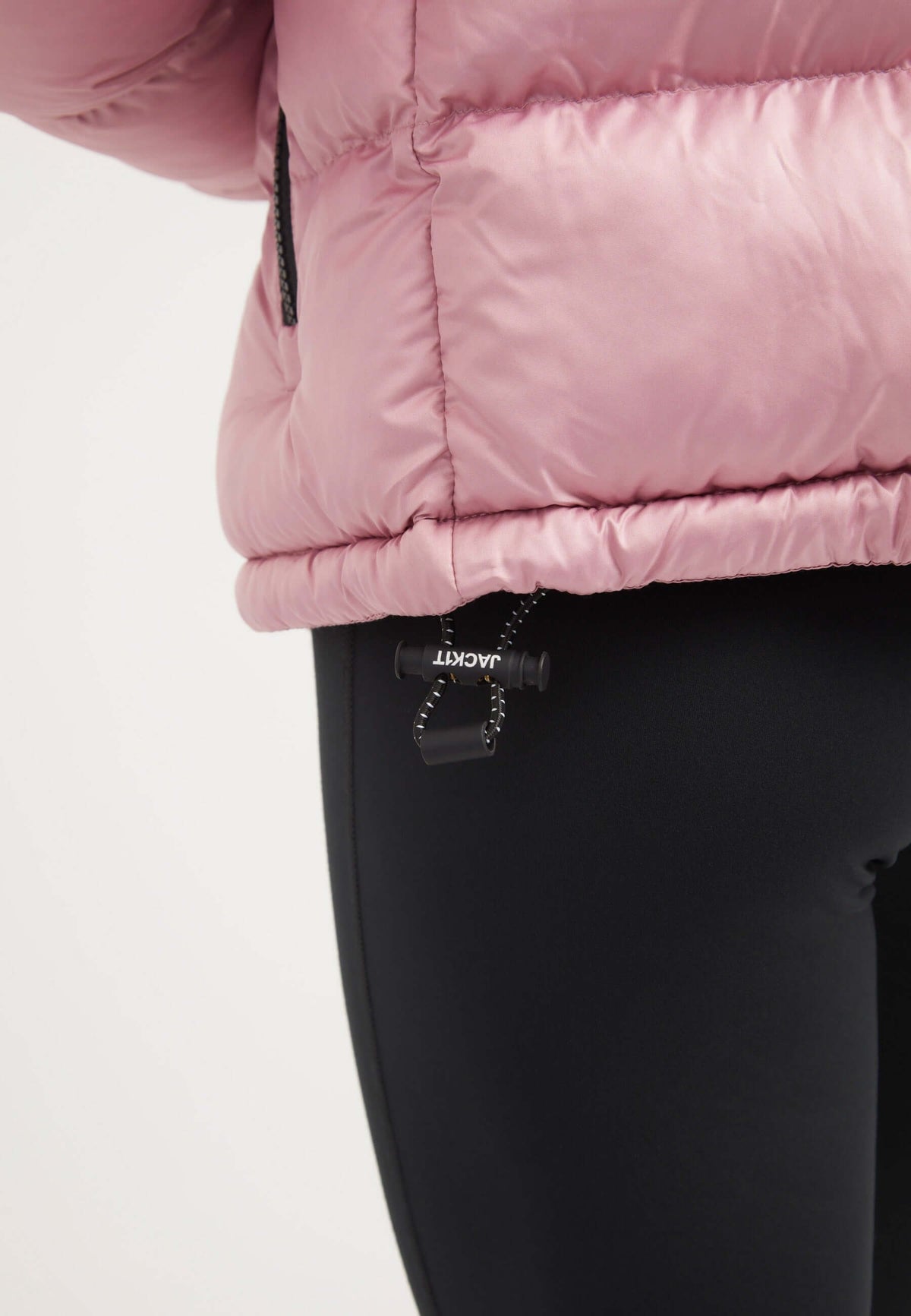 Close-up of a model wearing a powder pink funnel neck jacket with a tapered fit and black leggings.
