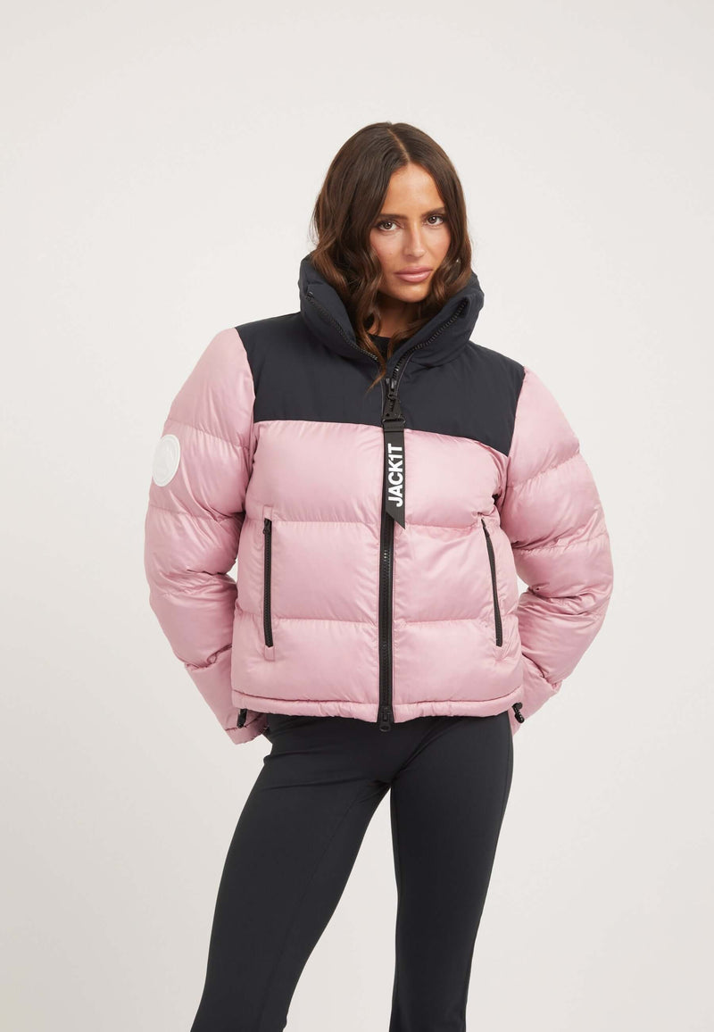 Woman wearing a tapered racer fit funnel neck jacket in powder pink and black with contrasting panels.