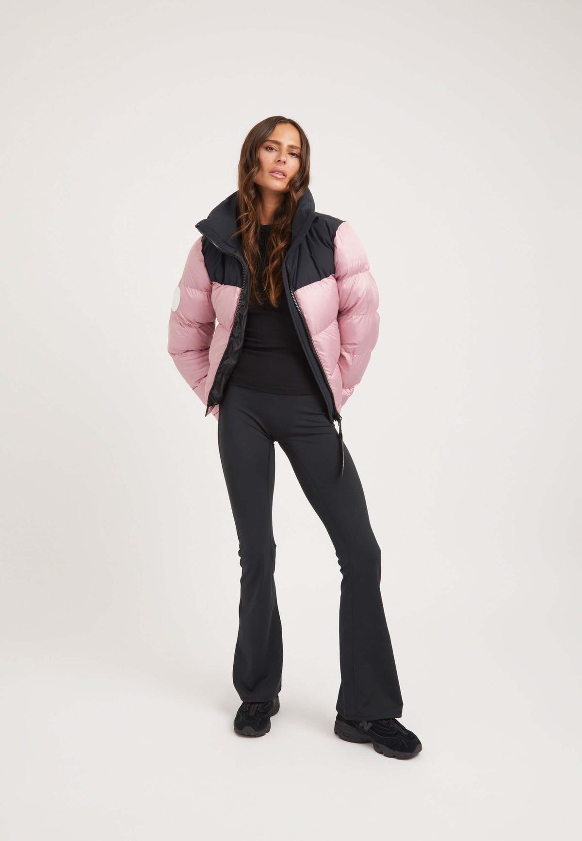 Model wearing a Funnel neck jacket in powder pink and black, paired with flared black pants.