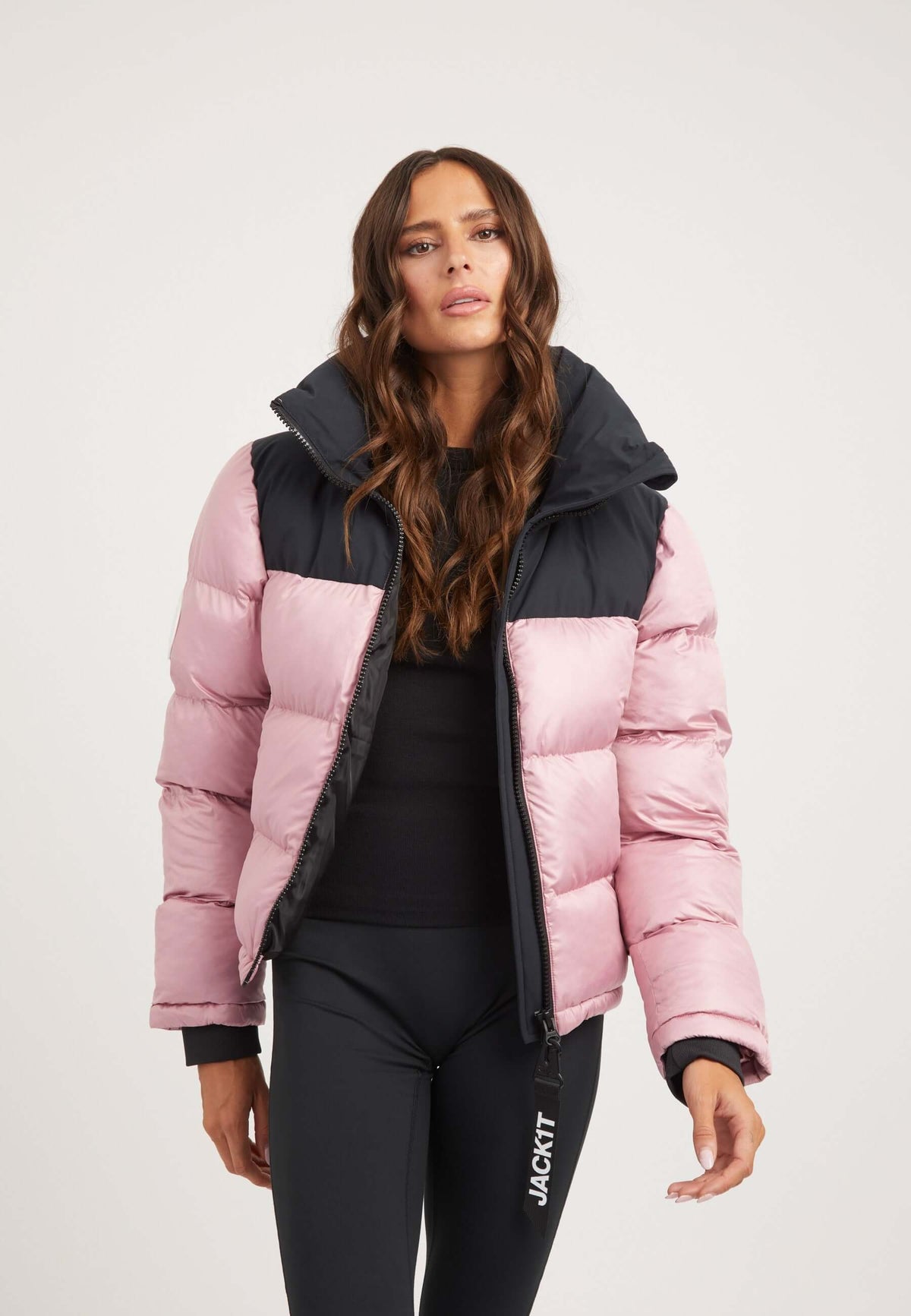 Model wearing a stylish funnel neck jacket in powder pink and black, showcasing premium synthetic insulation and a tapered racer fit.
