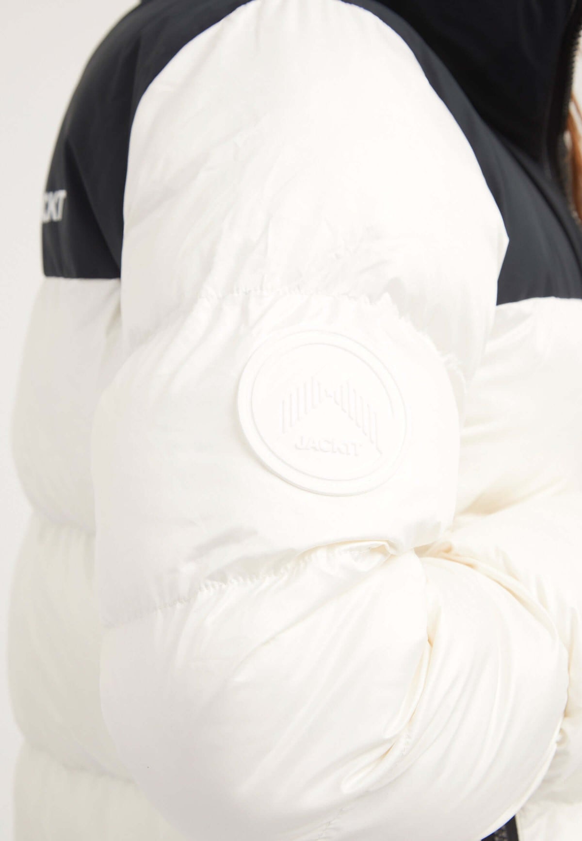 Detail of the funnel neck jacket with white puffy sleeve and logo on black fabric.
