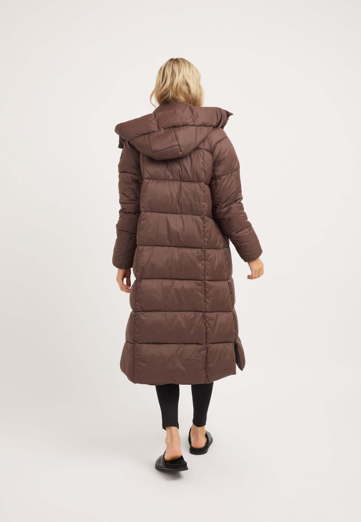 Back view of a woman wearing the Cloud Boss Coat Mid Brown, a womens long puffer coat with removable hood and side splits.