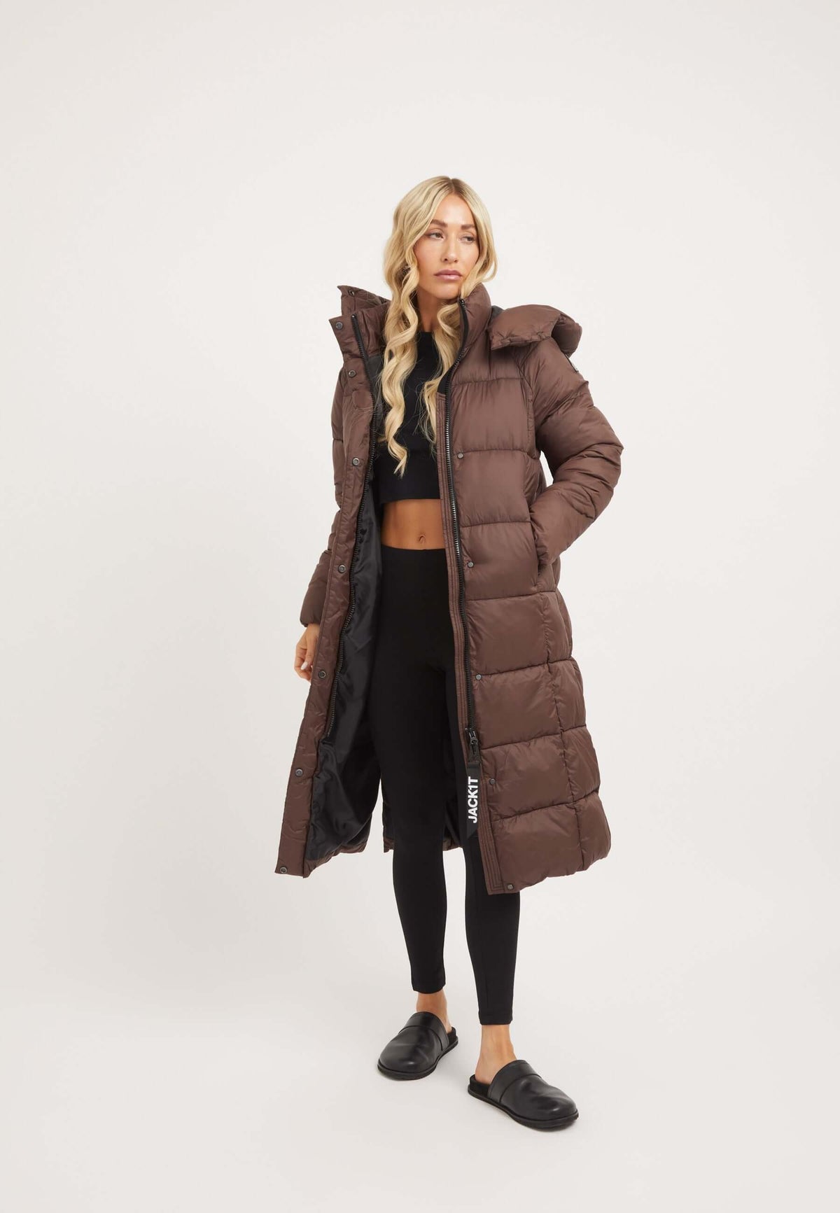 Womens long puffer coat in mid brown with hood, worn by model standing against a light background.