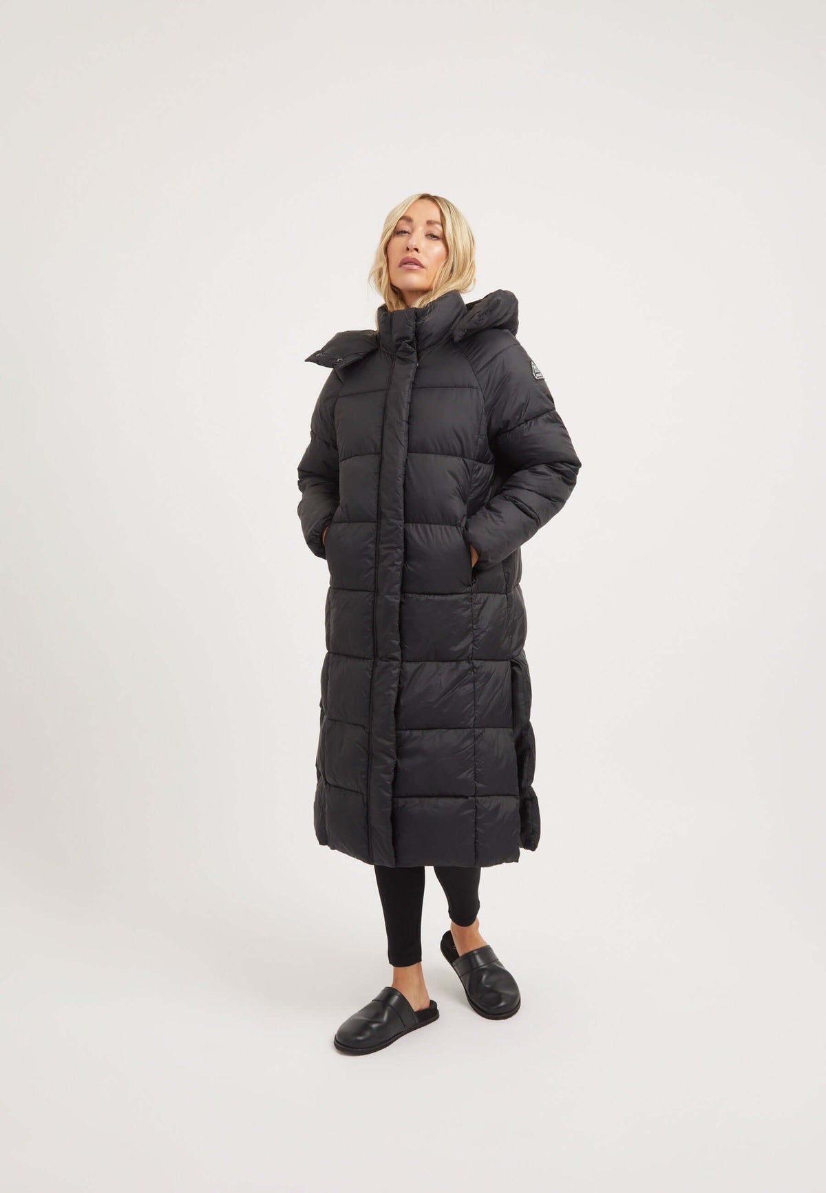 Model wearing the Cloud Boss Coat Black, a womens long puffer coat, featuring a full length silhouette and removable hood.