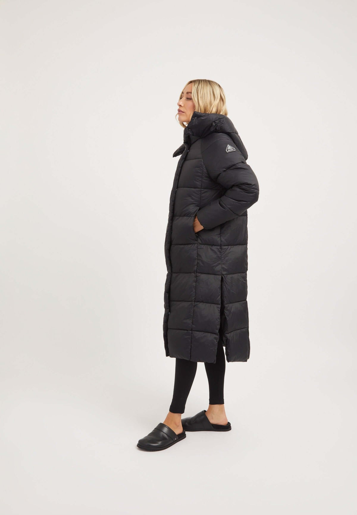 Model wearing the Cloud Boss Coat Black, a womens long puffer coat, showcasing its full length silhouette and removable hood.