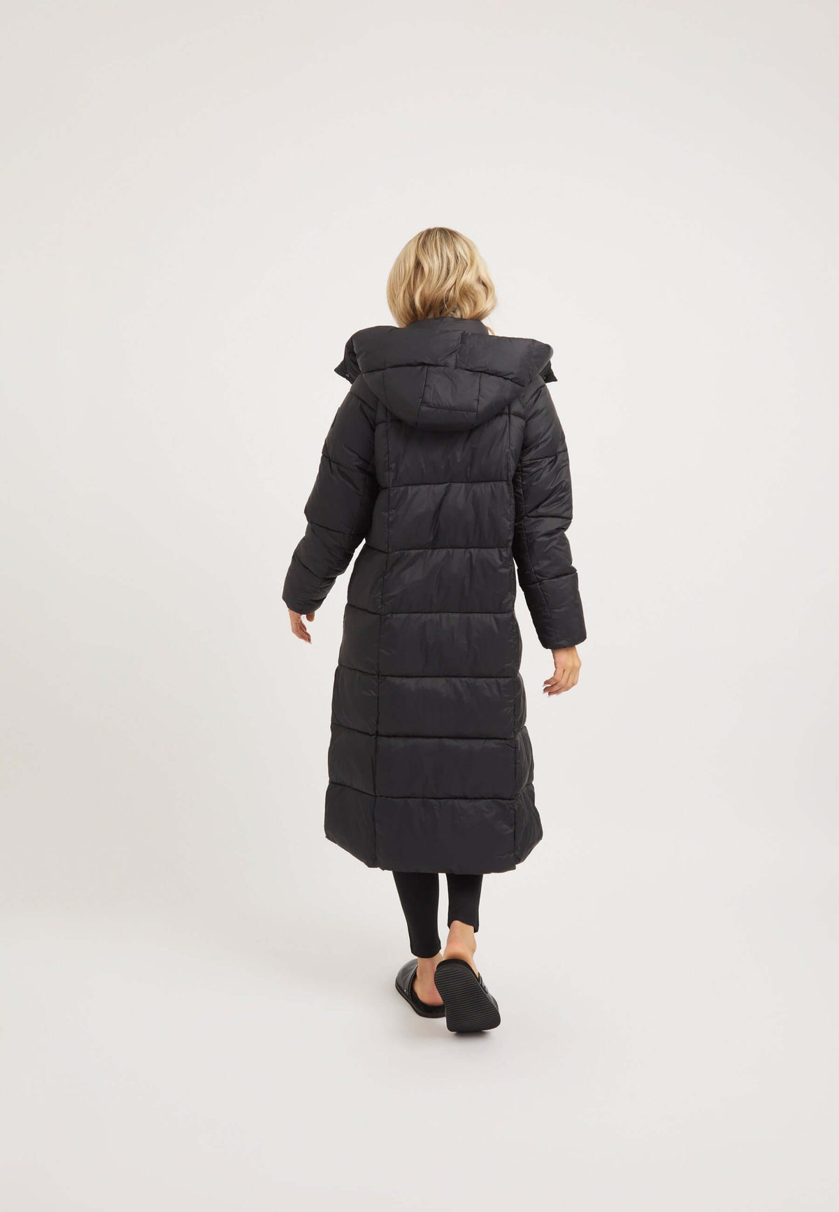 Back view of a woman wearing a Cloud Boss Coat Black, a womens long puffer coat, featuring a hood and full length design.
