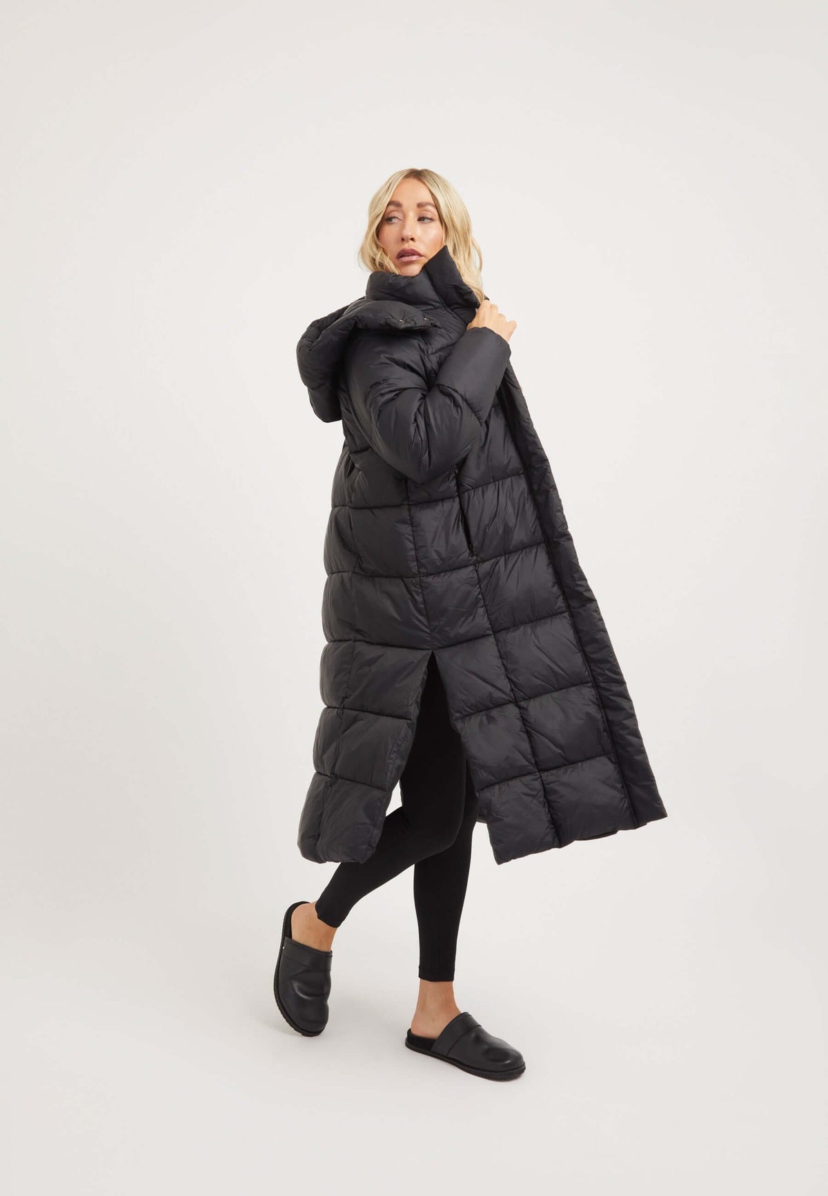 Model wearing a womens long puffer coat in black with removable hood and side split opening.
