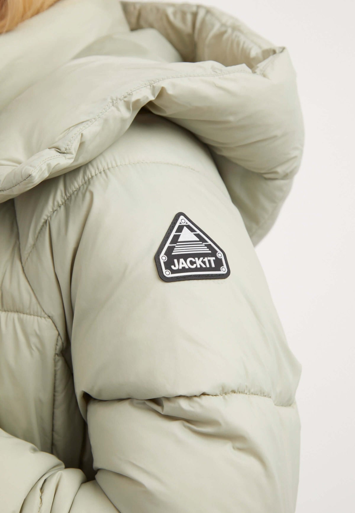 Close-up of the Cloud Boss Coat in sage with a reflective badge on the arm, showcasing a stylish womens long puffer coat.