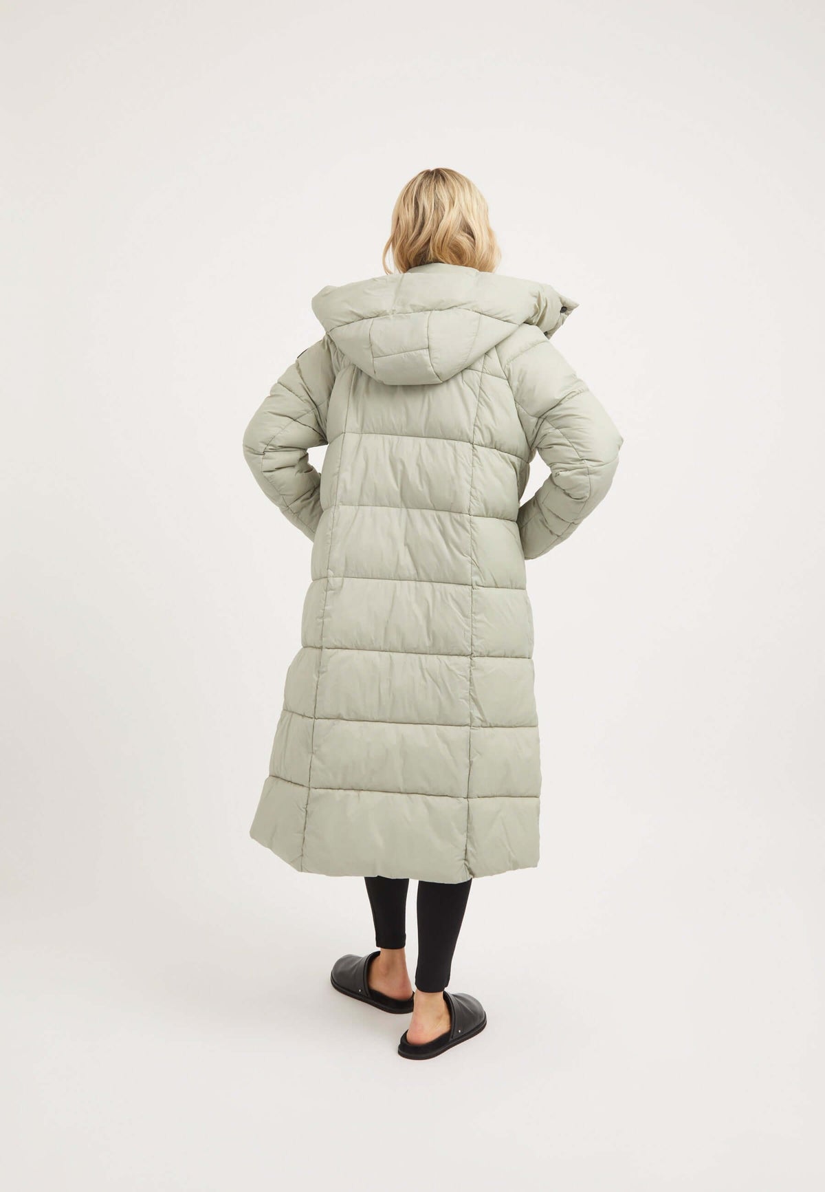 Back view of a model wearing a Cloud Boss Coat in Sage, showcasing the womens long puffer coat with a removable hood.