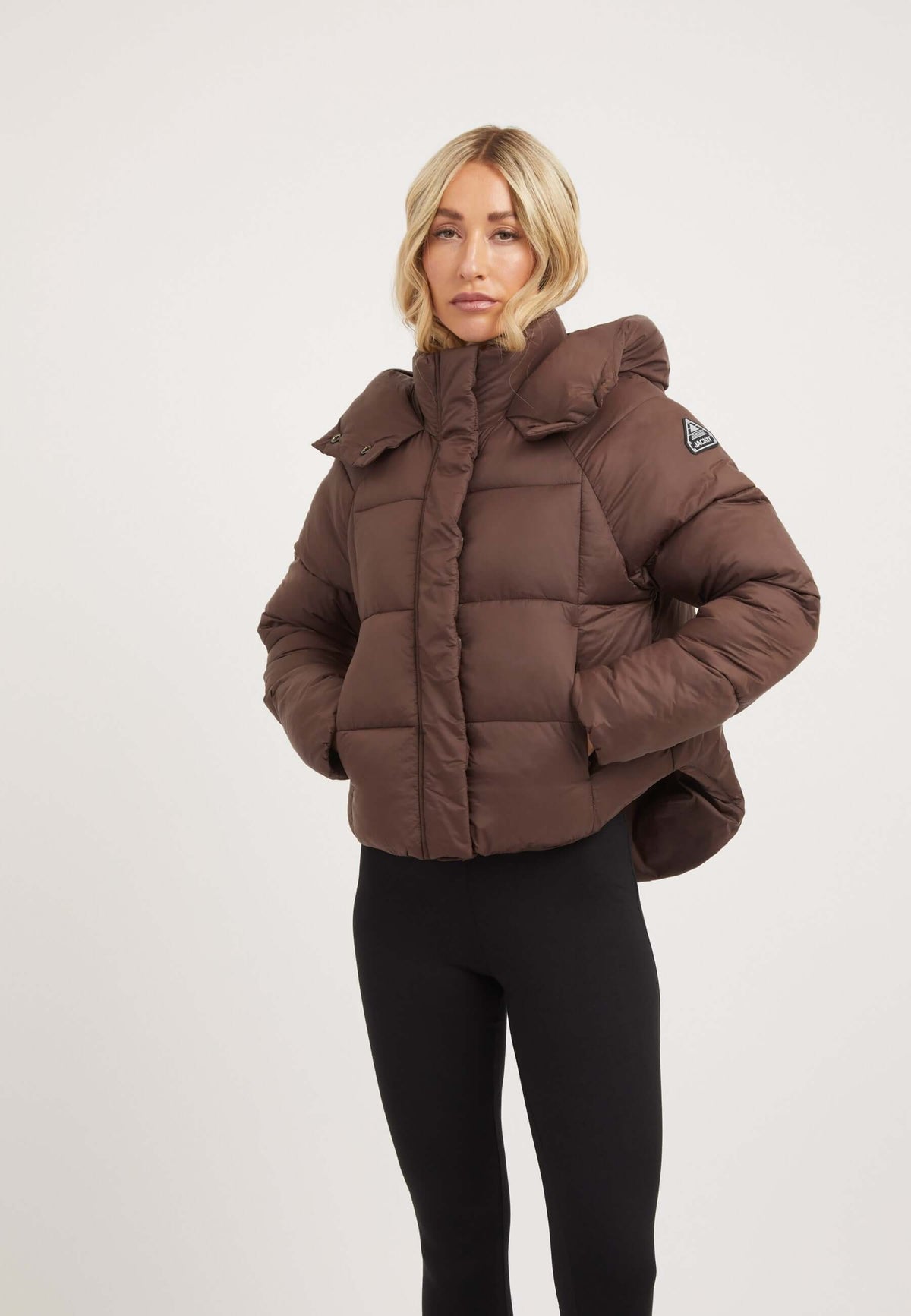 Short puffer jacket women in mid brown with adjustable hood and modern cropped cut.
